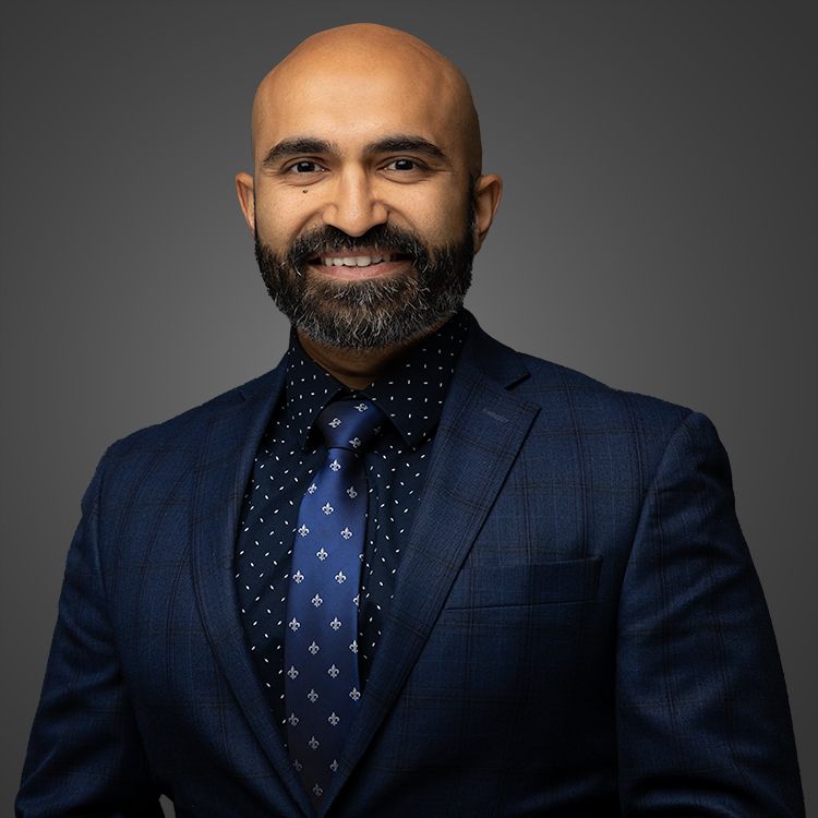 Professional portrait of person in navy suit with polka dot tie against dark background.