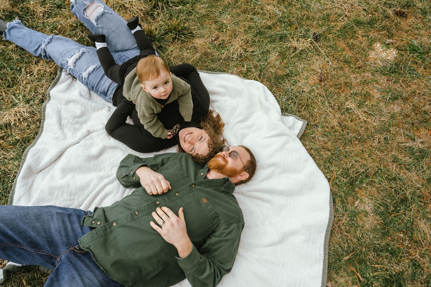 A couple relaxes together on a white blanket in the grass during a sunny autumn day.