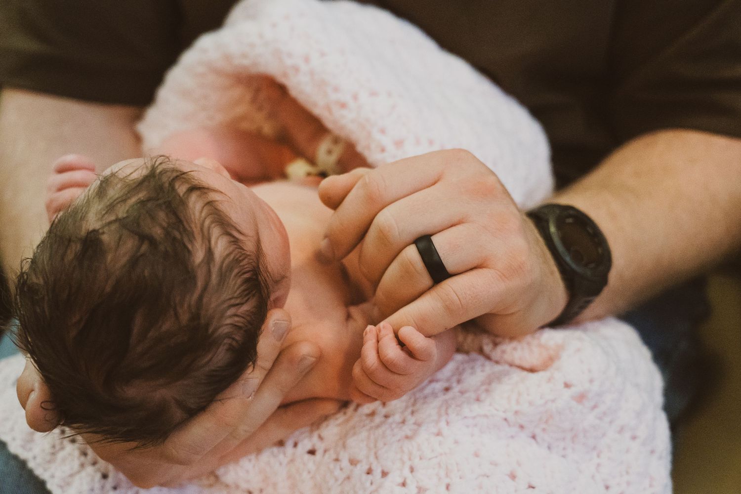 A sleeping baby lies peacefully on white bedding while being gently touched by an adult hand.