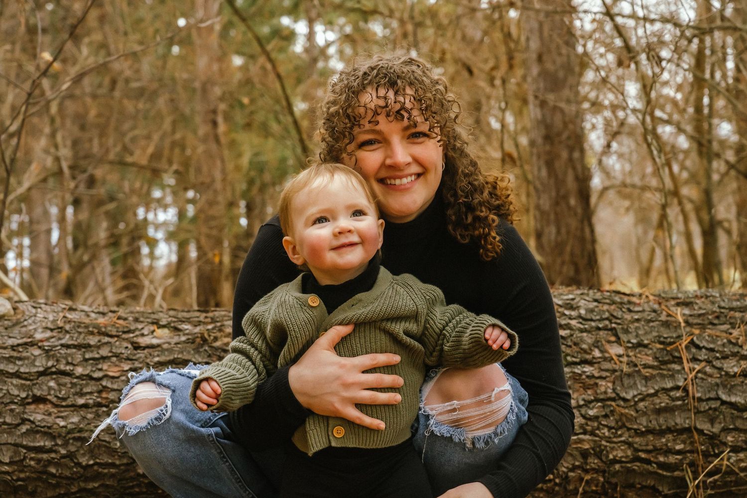 A candid outdoor family photoshoot in a wooded area during autumn with natural lighting and fallen leaves.