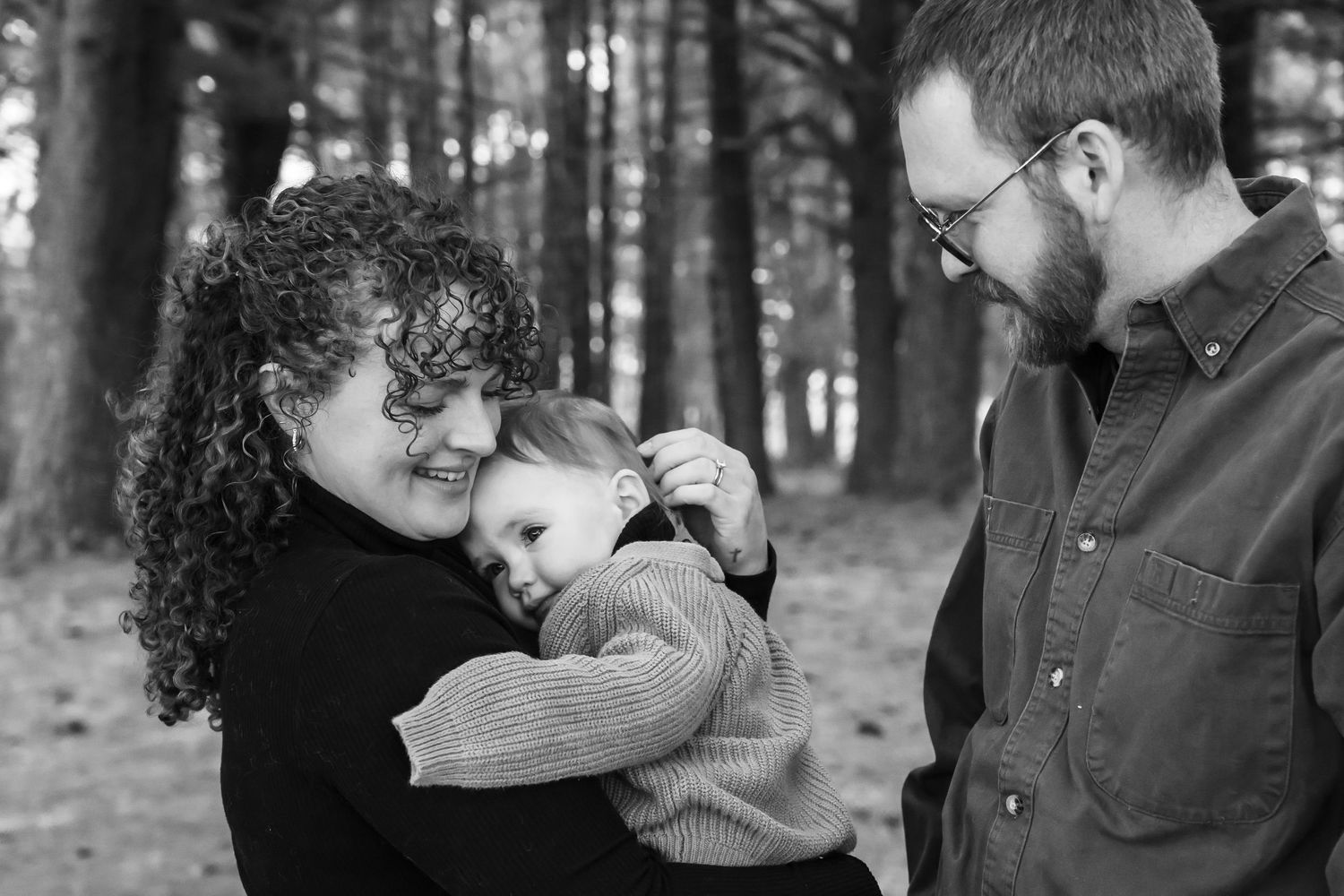 A series of black and white photos showing tender family moments in an outdoor wooded setting.