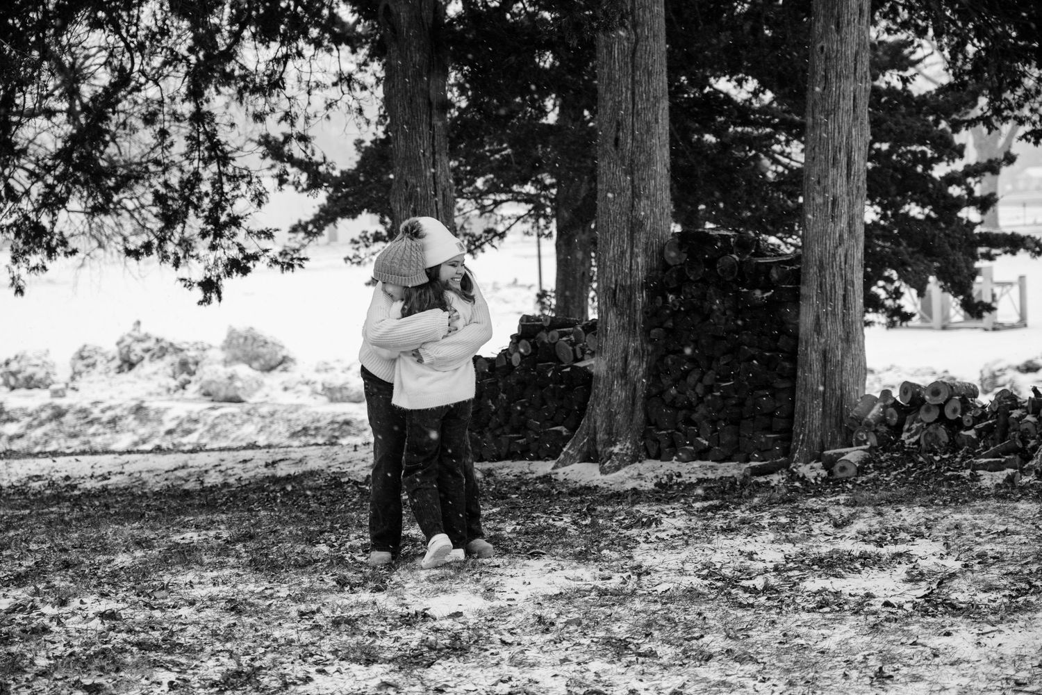 A black and white winter photo of someone holding a snowball among tall evergreen trees.