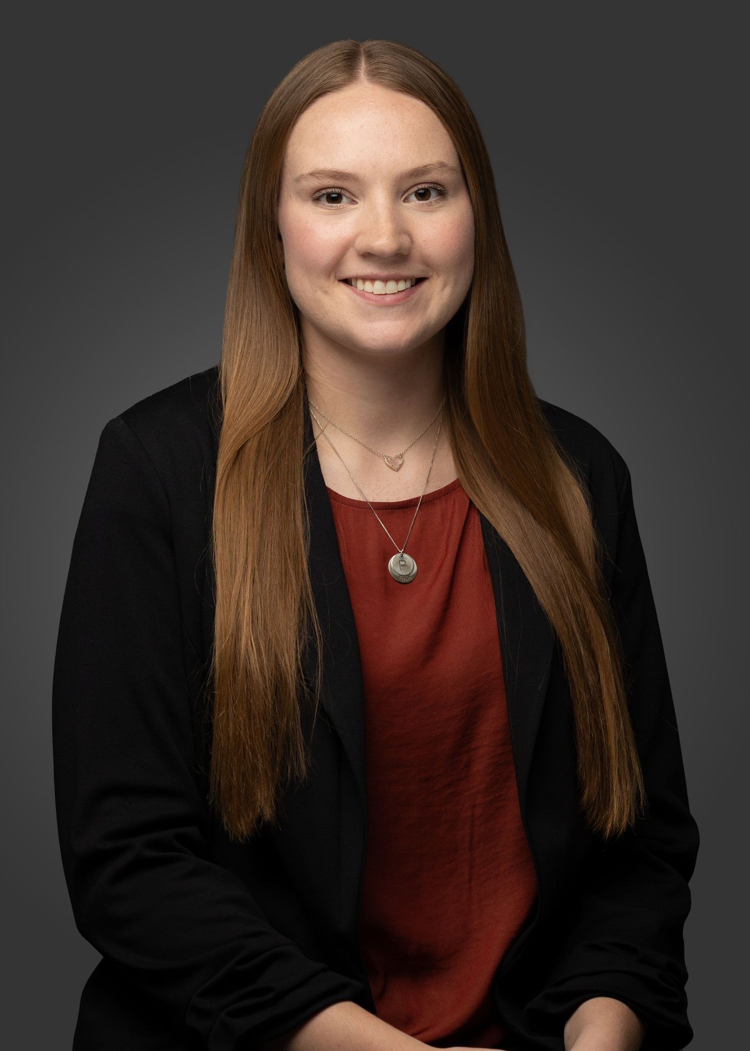 Professional studio portrait against dark background wearing black blazer and red top.