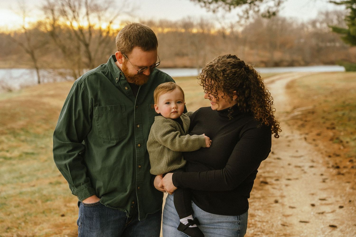 A family enjoys a tender moment together on a path covered in autumn leaves during golden hour.
