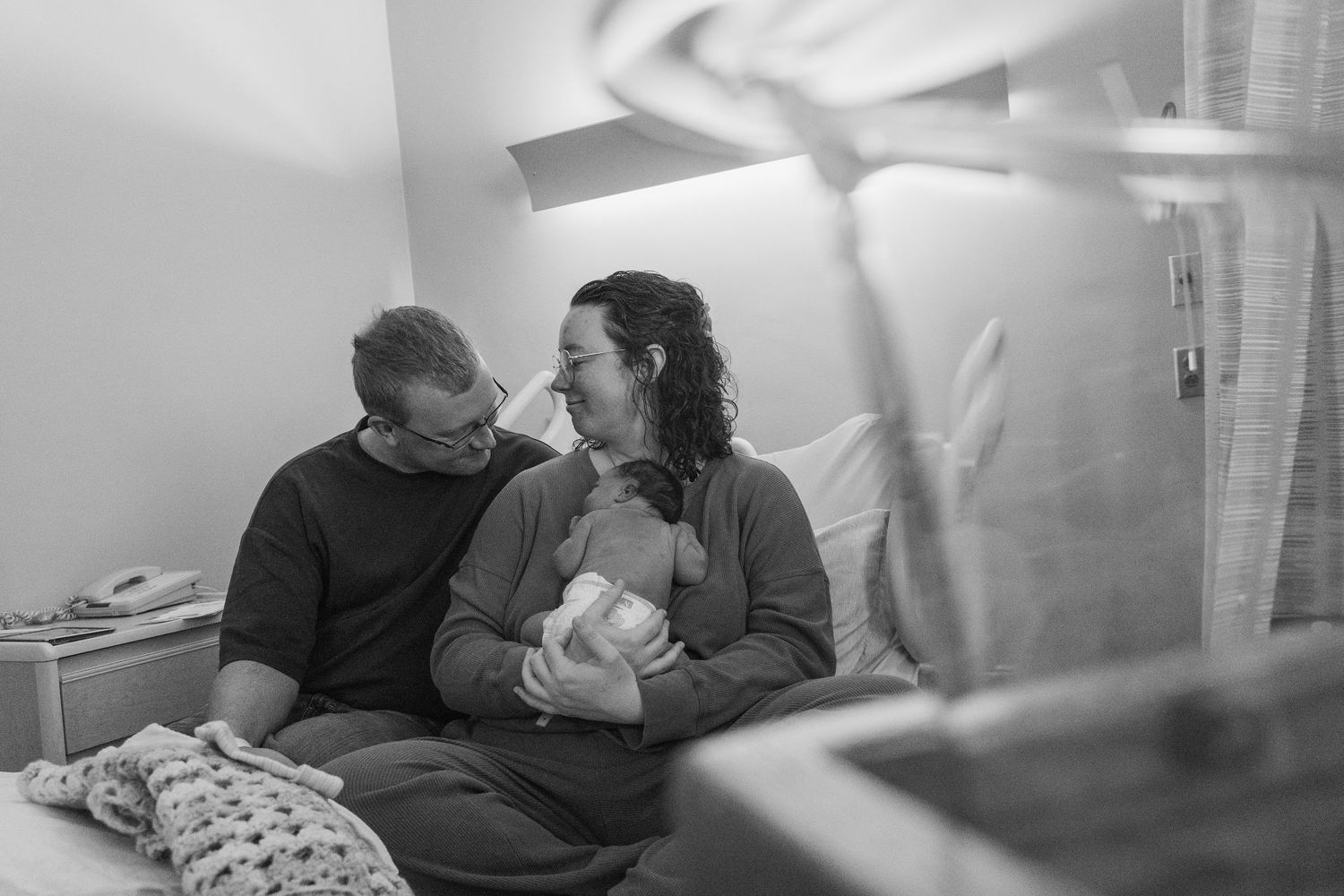 Intimate black and white hospital photo of new parents sharing a quiet moment together.