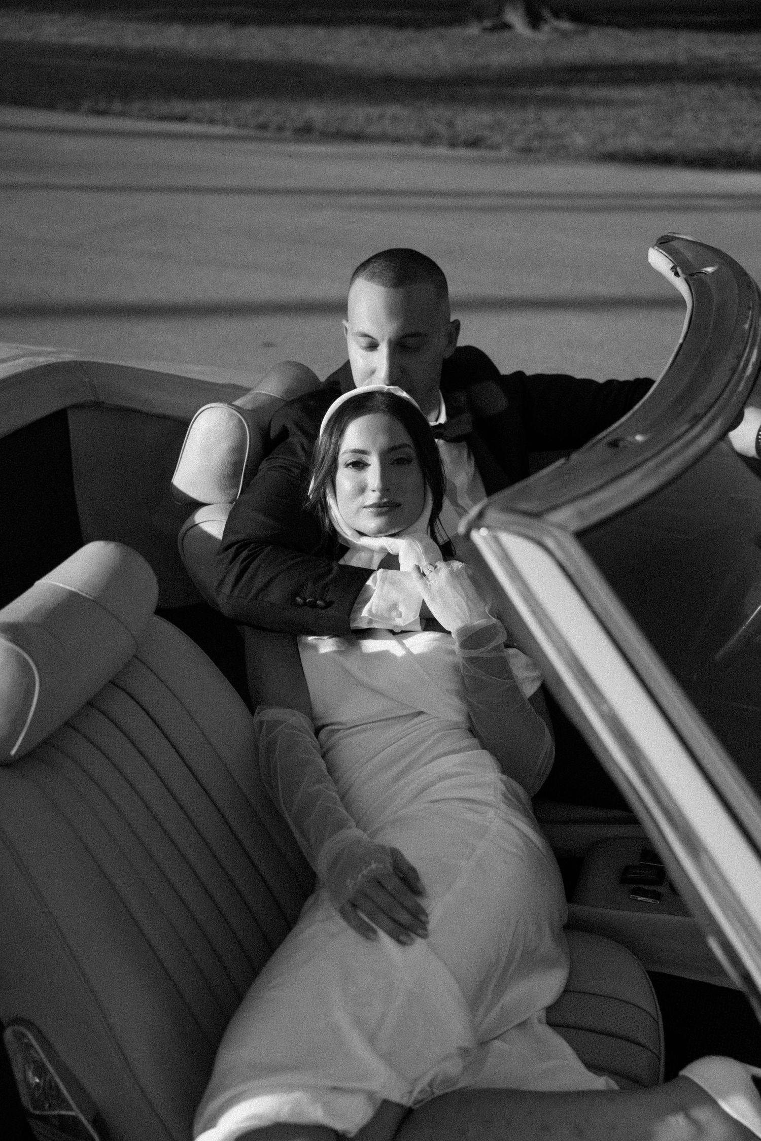 A romantic black and white photo of a couple lounging in the back seat of a vintage convertible car.
