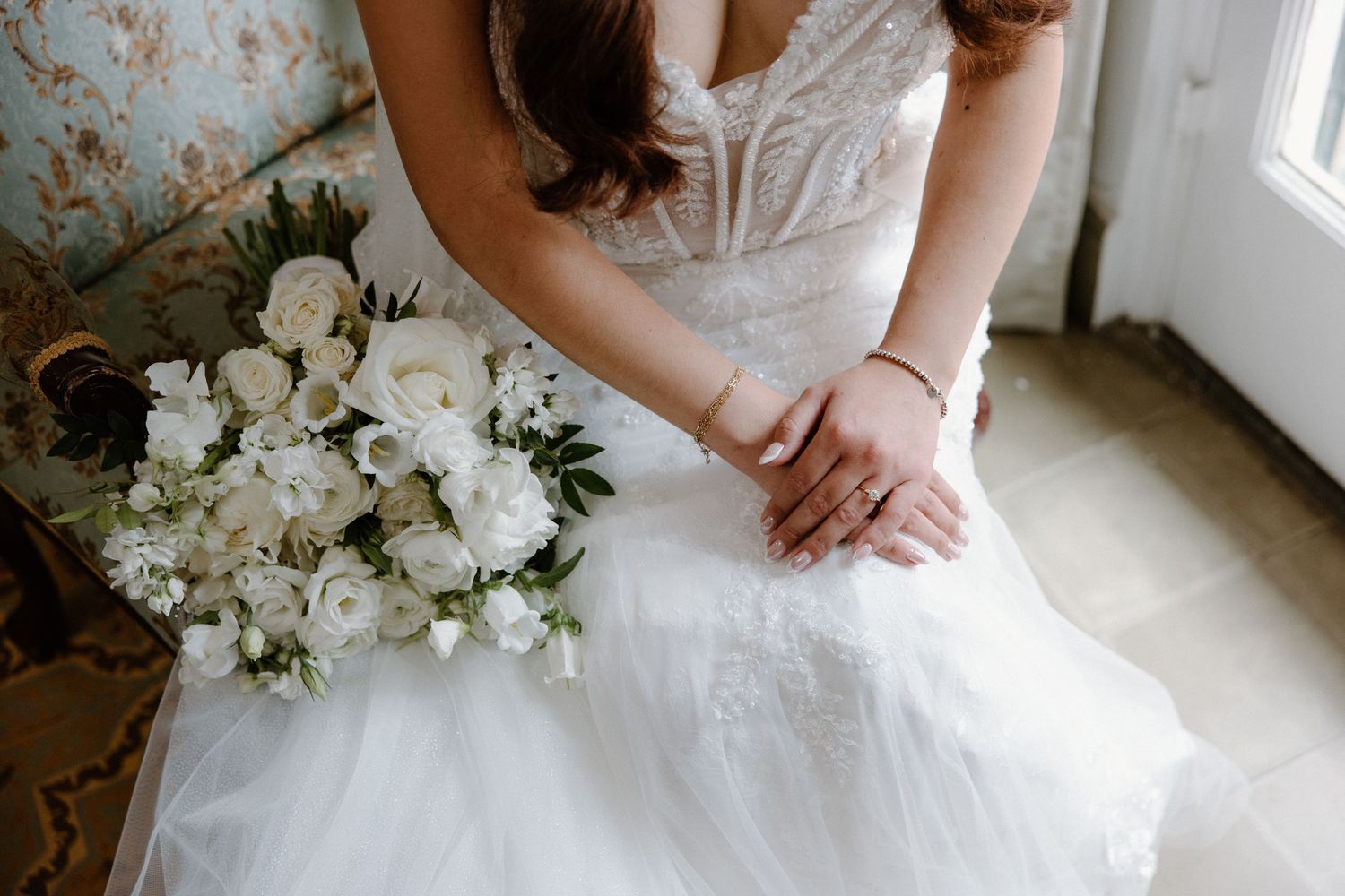 A close-up view of a white wedding dress with delicate lace details and a beautiful bridal bouquet near a window.