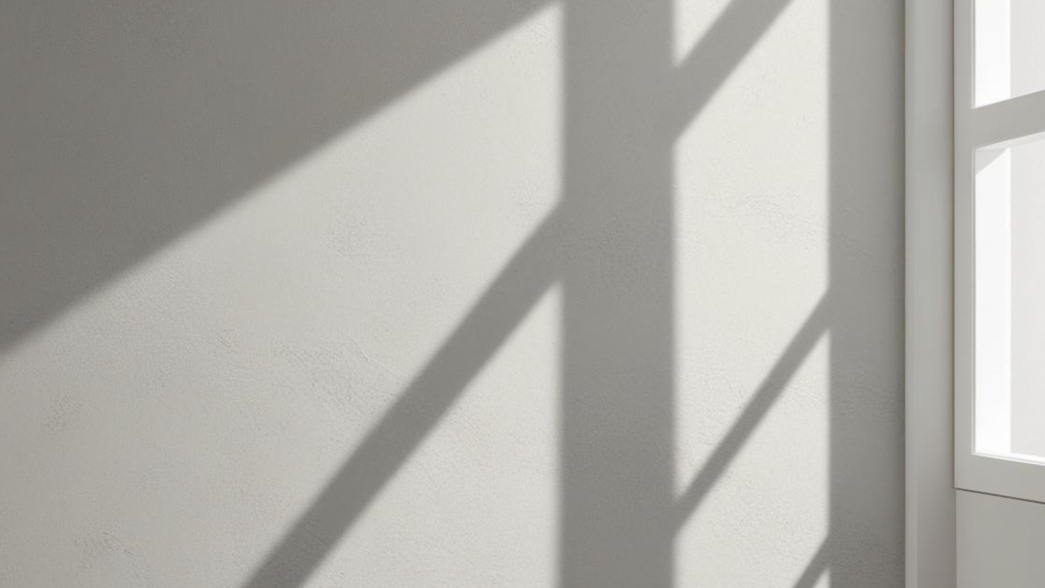 Diagonal shadows cast dramatic lines across a minimalist white interior wall.