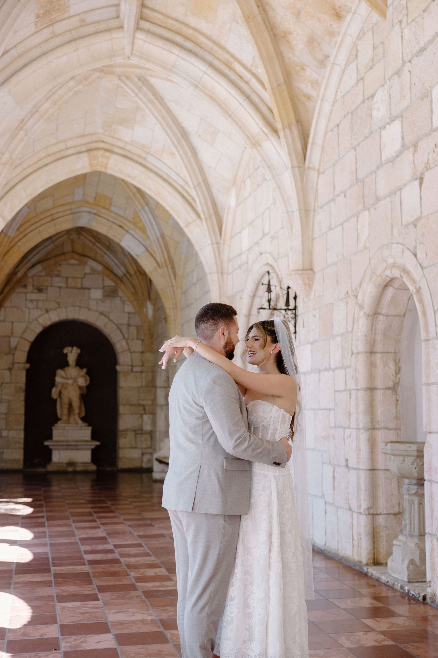 A romantic wedding photo sequence in a stone archway corridor showing a couple sharing intimate moments in light attire.