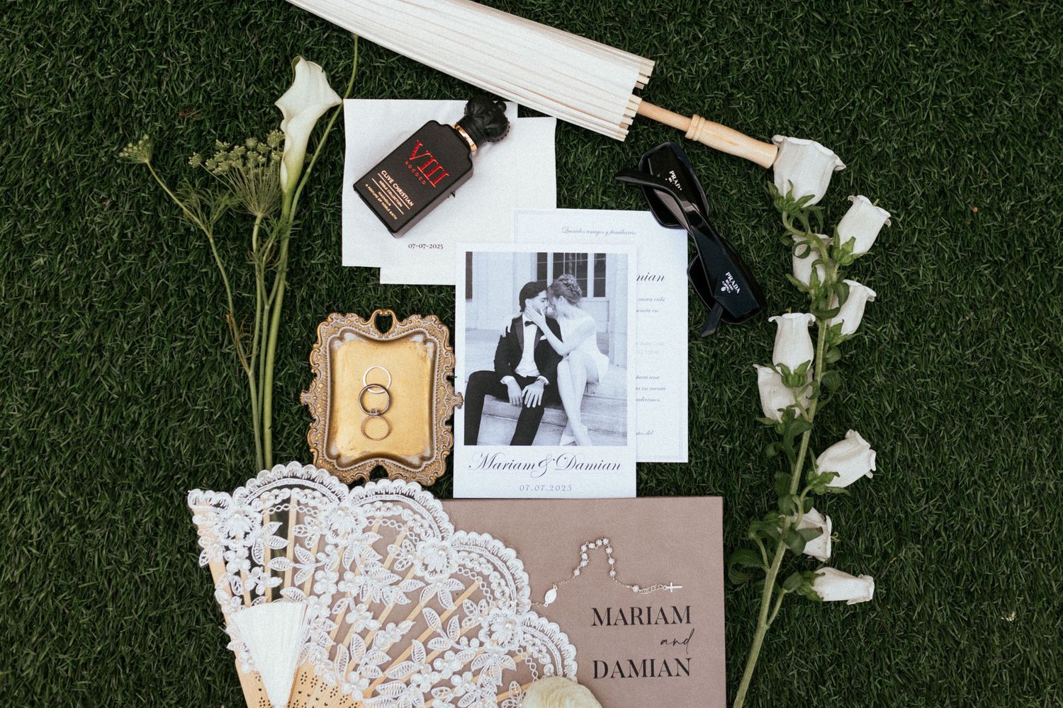 Wedding invitation suite with delicate lace details and floral elements laid out on dark green grass background.