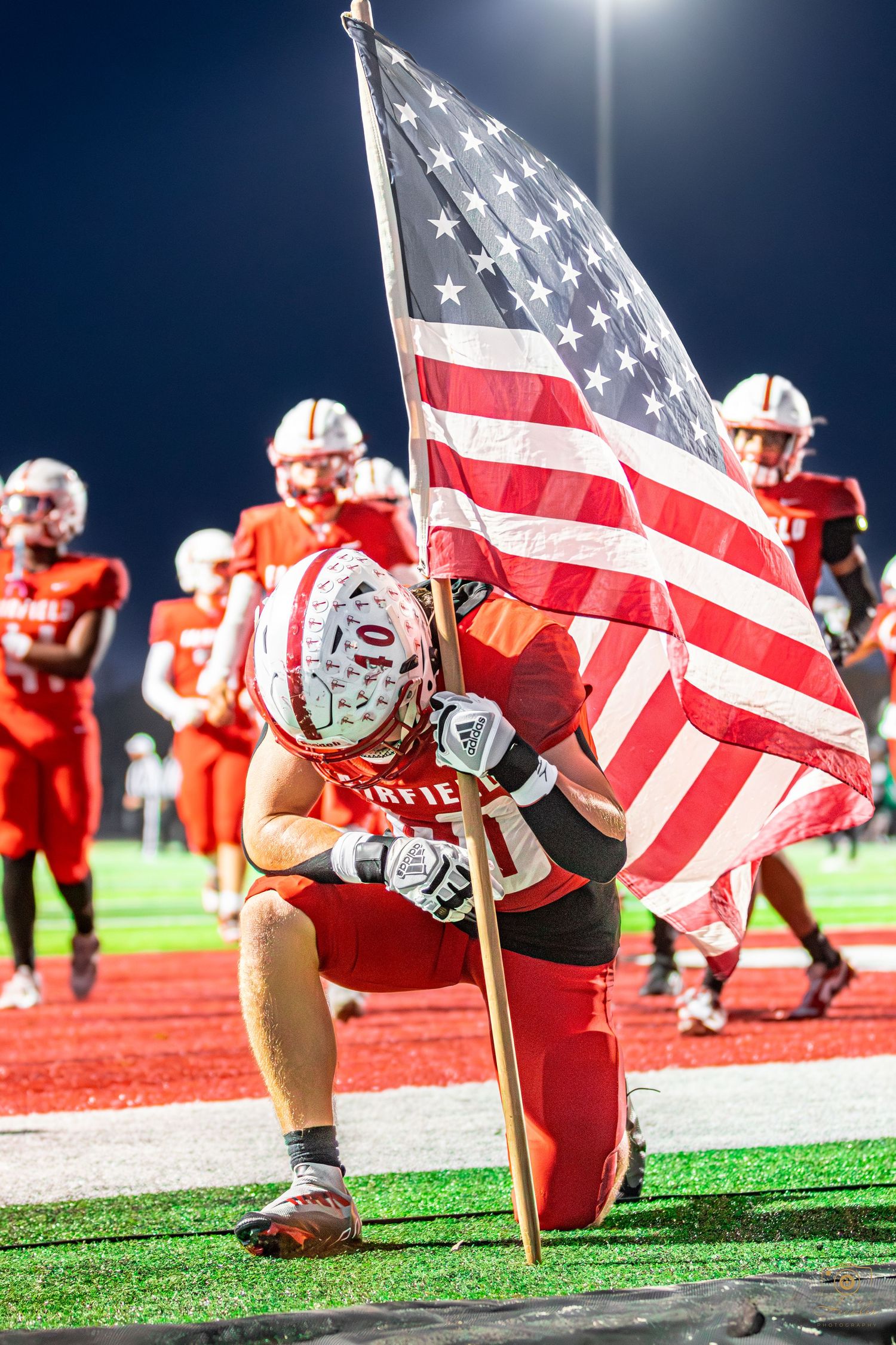 Football player holding up American flag while praying pregame.