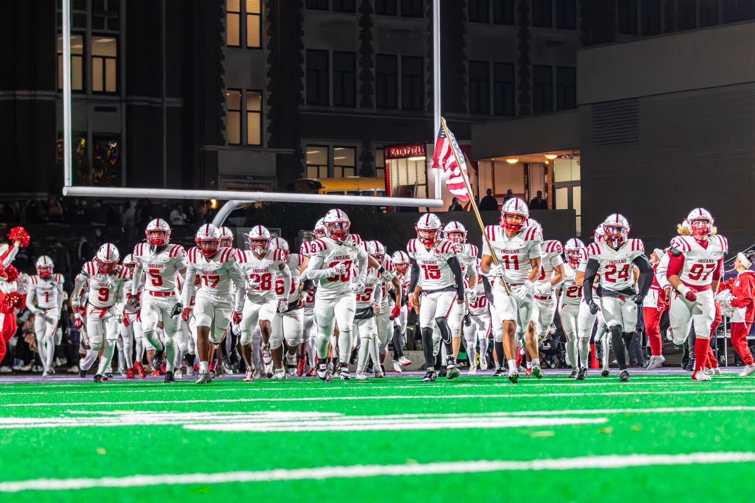 Football team running out with a senior running with American flag for the last time of the season.