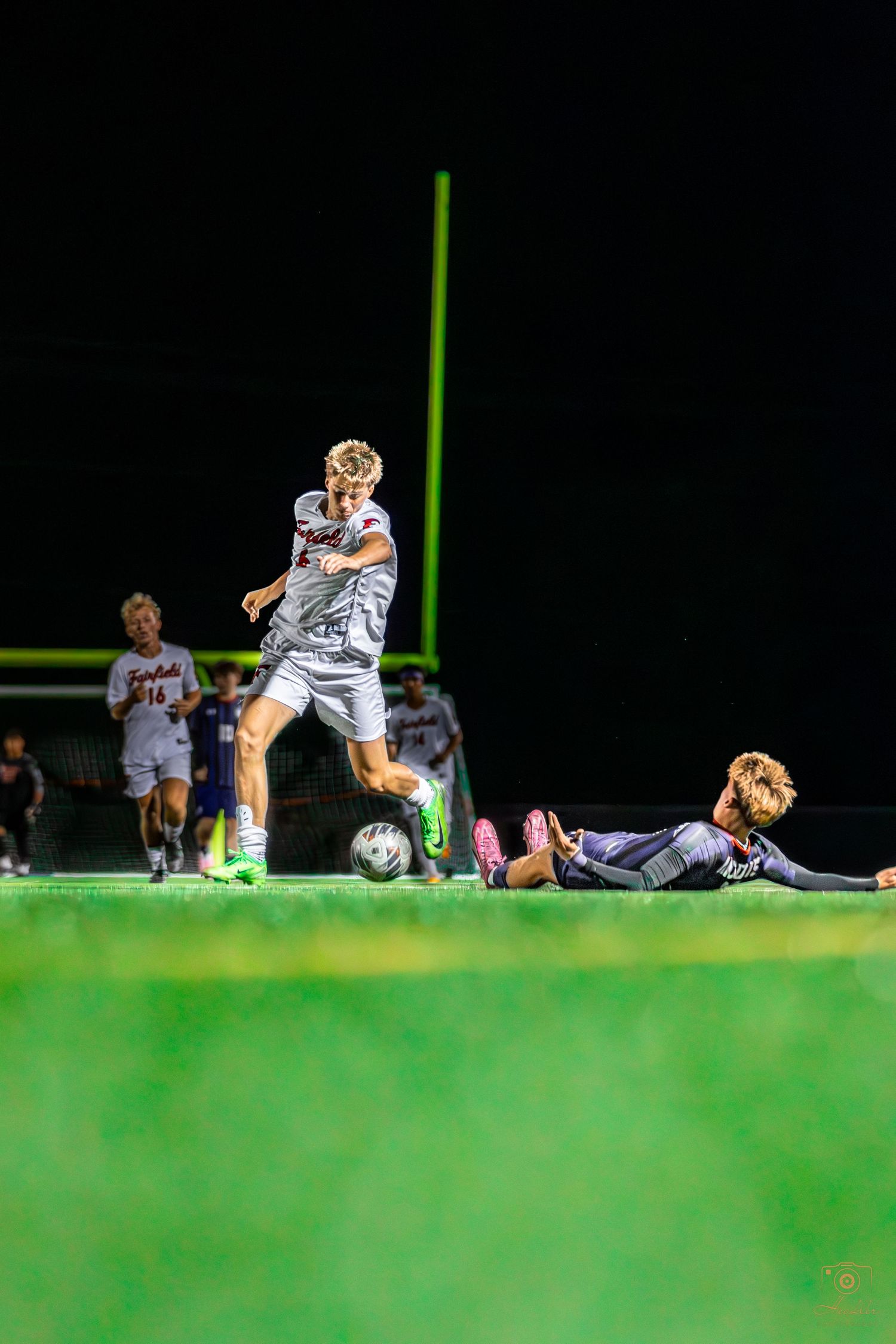 Soccer player with ball while opposing player is on the ground.