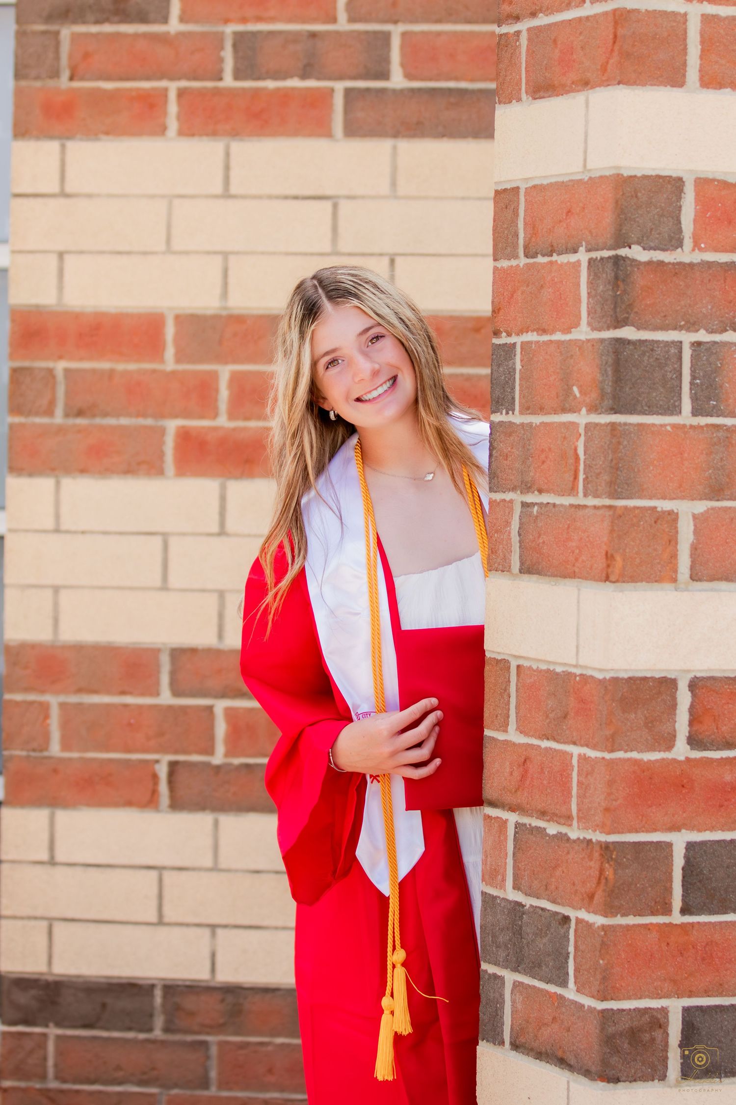 Senior with cap and gown looking around a wall.