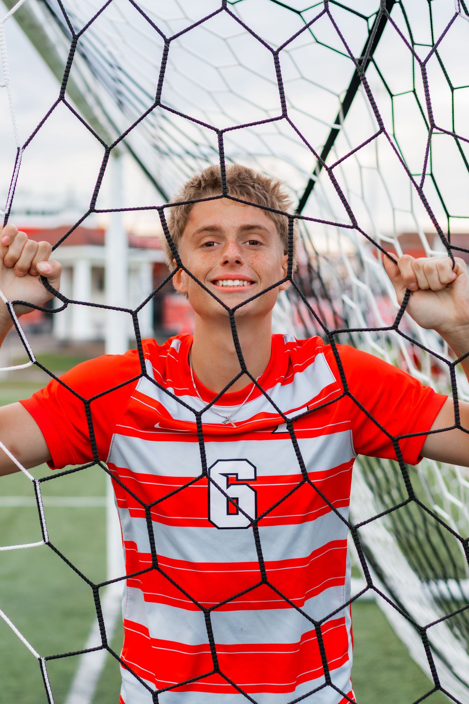 Soccer senior smiling through soccer goal.