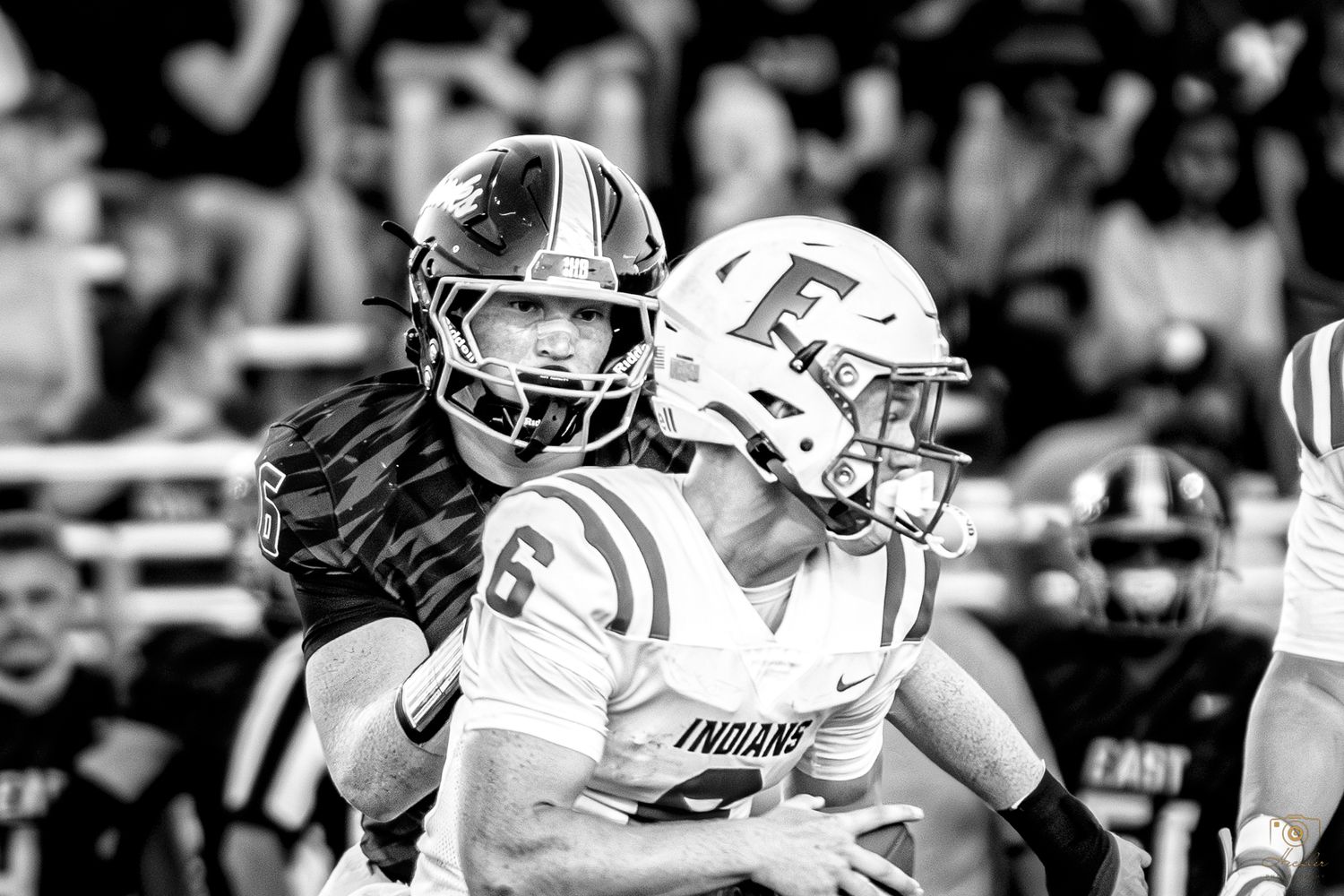 Football player running towards quarterback in focas while the quarterback in out of focas about to get sacked.
