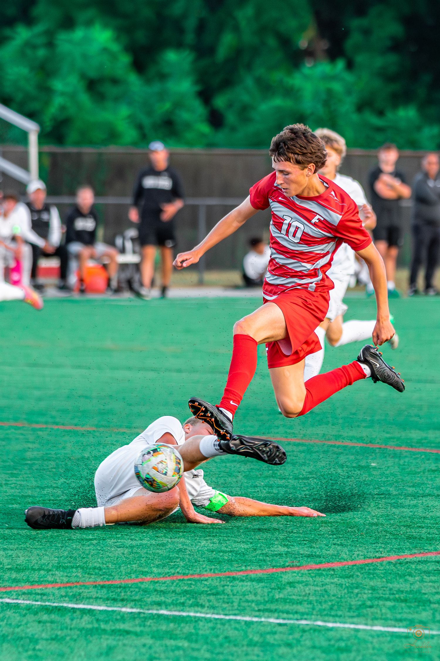 Soccer player jumping over player with ball.