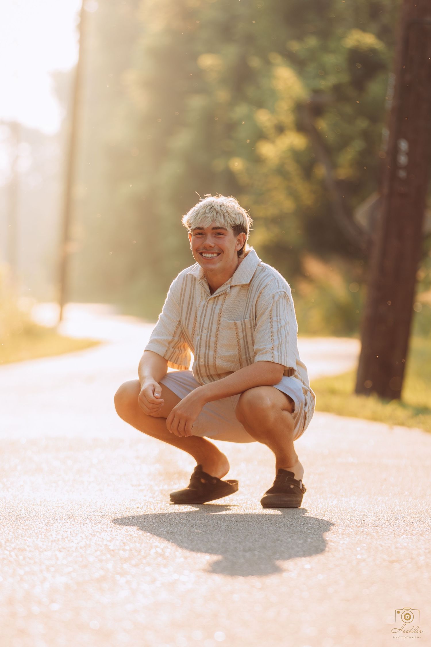 Senior crouching down smiling at camera with the sun in the background.