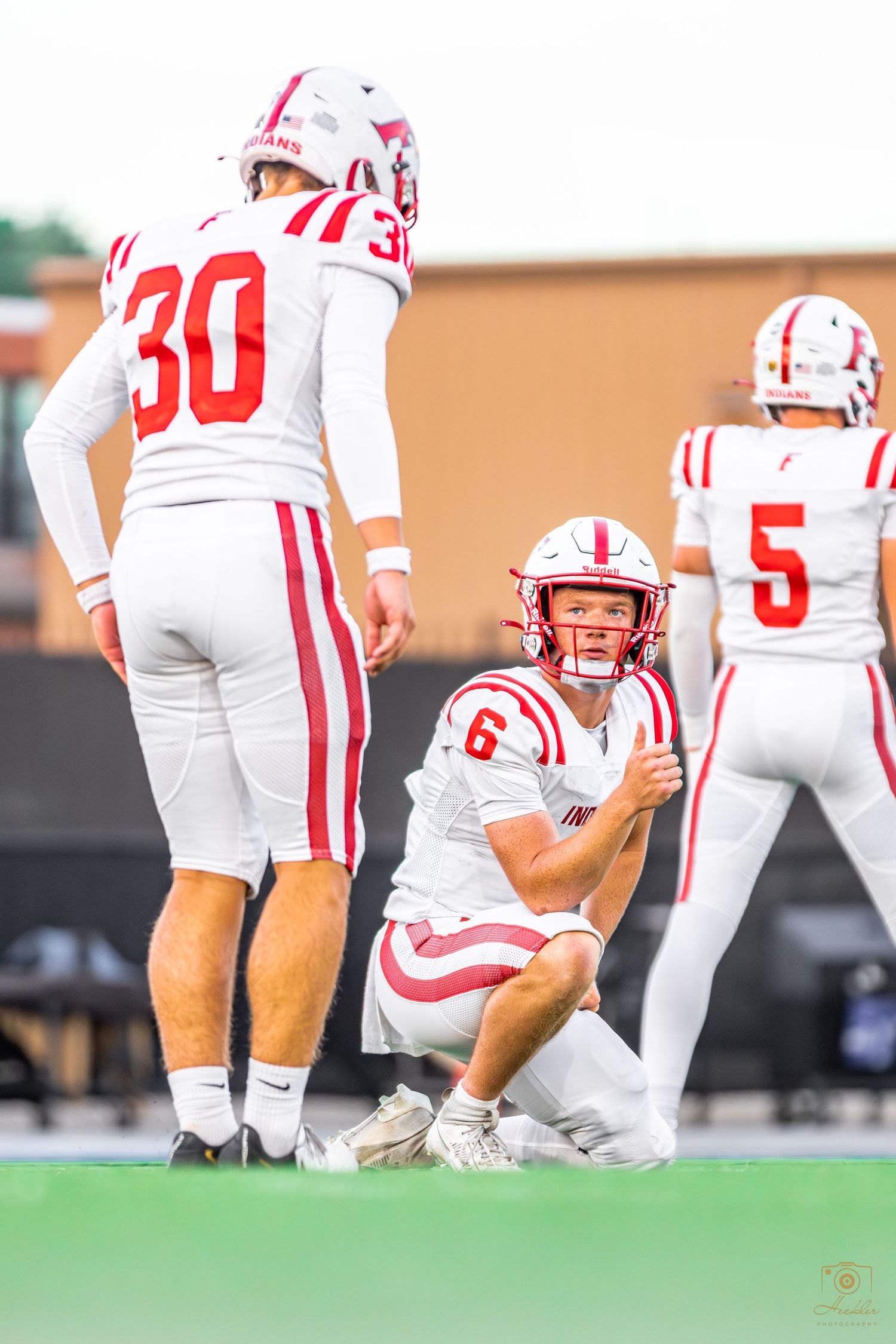Football player about to snap the ball to the kicker as he thumbs up to the kicker.