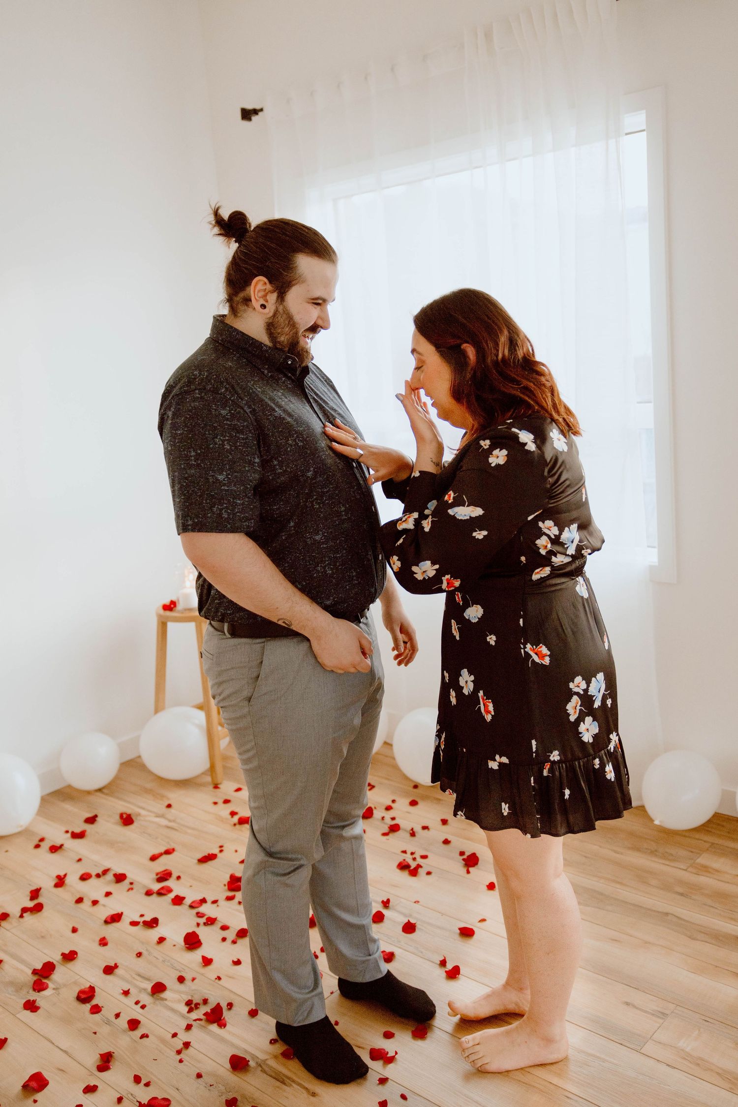 Couple reacting emotionally on floor scattered with red rose petals and white balloons.