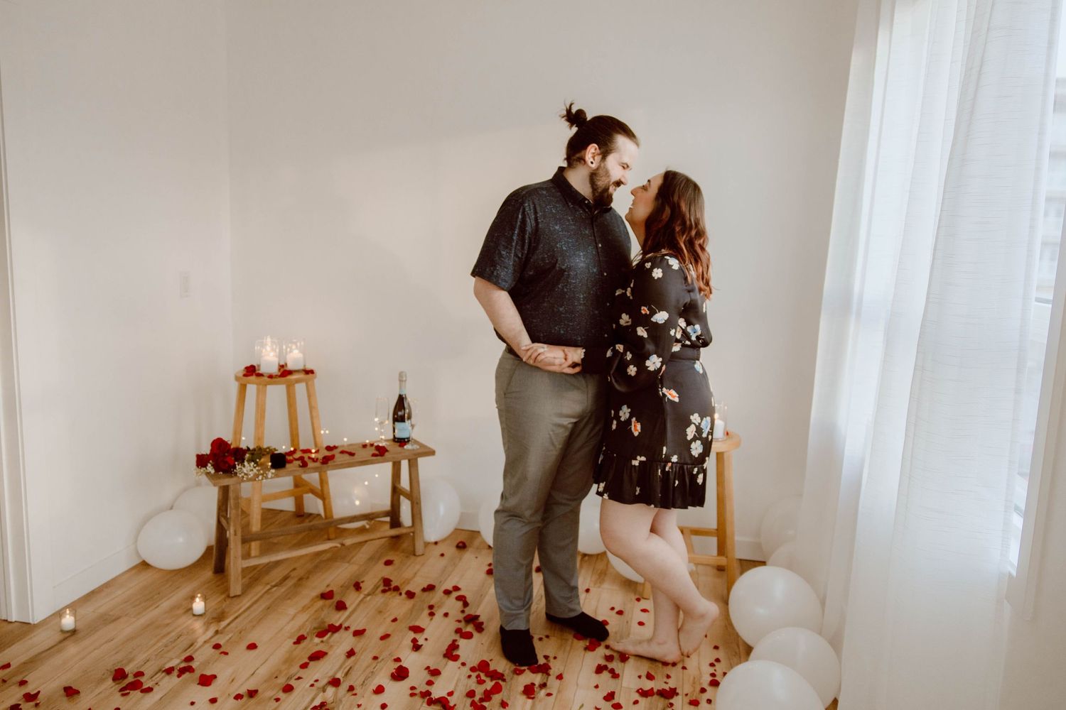 Couple posing in minimalist room decorated with rose petals and white balloons.