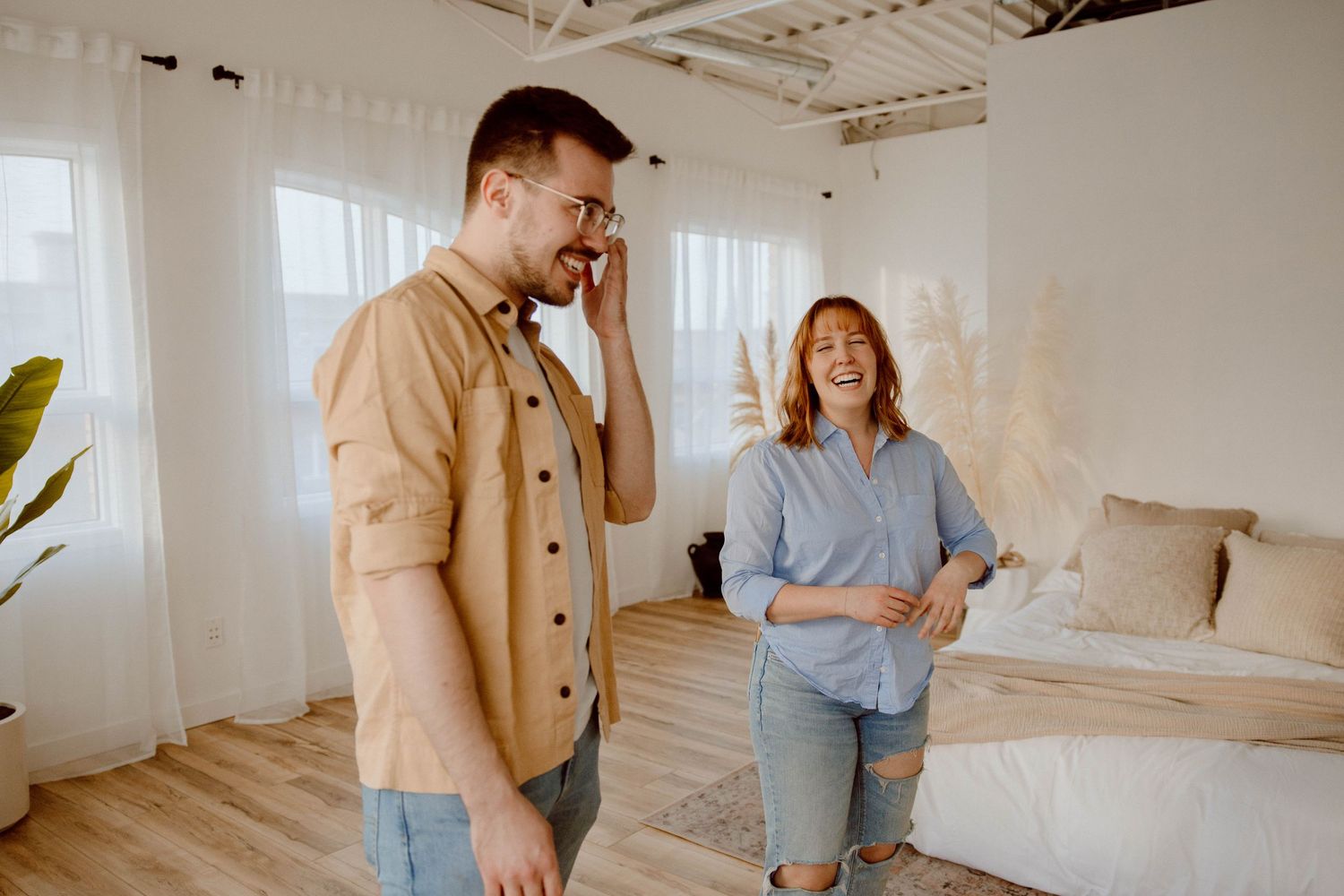 Two people sharing light-hearted moment in bright, minimalist room with houseplants.
