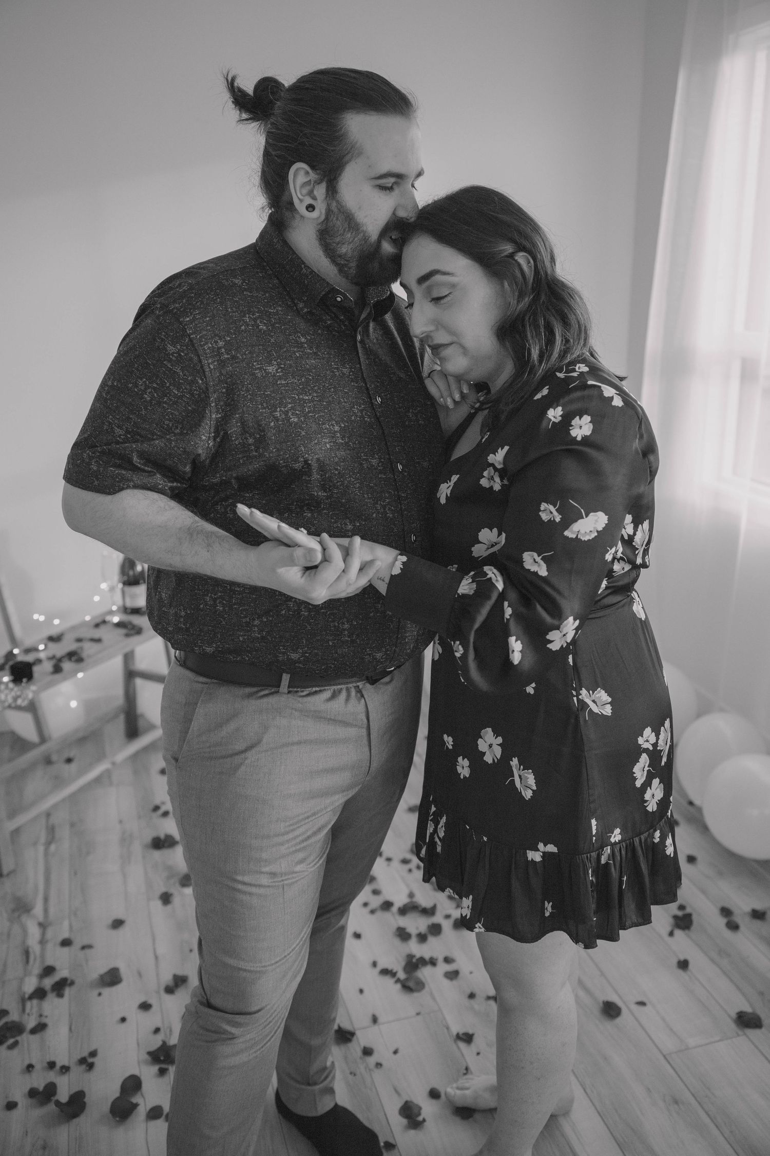 Black and white photo of couple sharing intimate moment surrounded by rose petals.