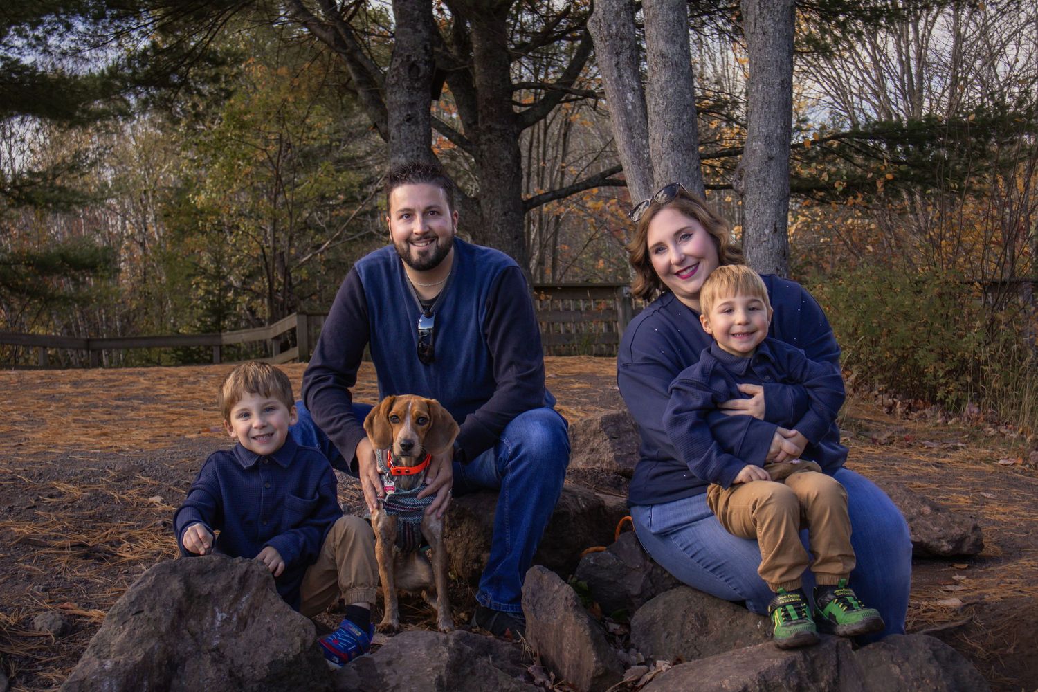 A group sits together with their brown dog on large rocks in an autumn outdoor setting.