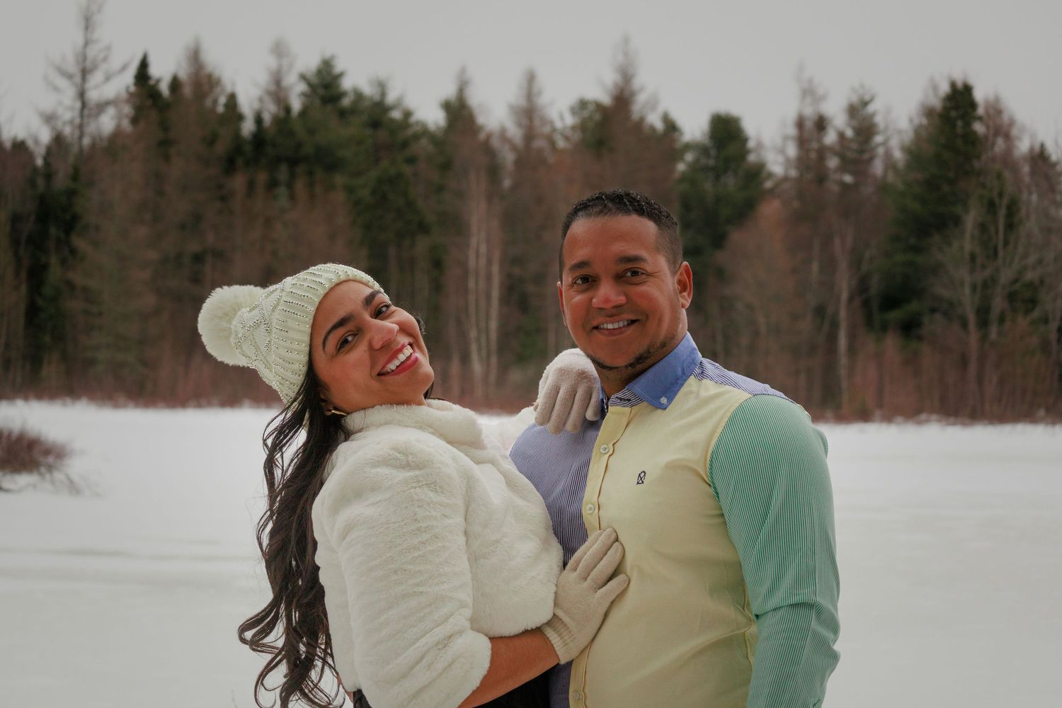 Couple in casual winter attire embracing near a snowy lake.