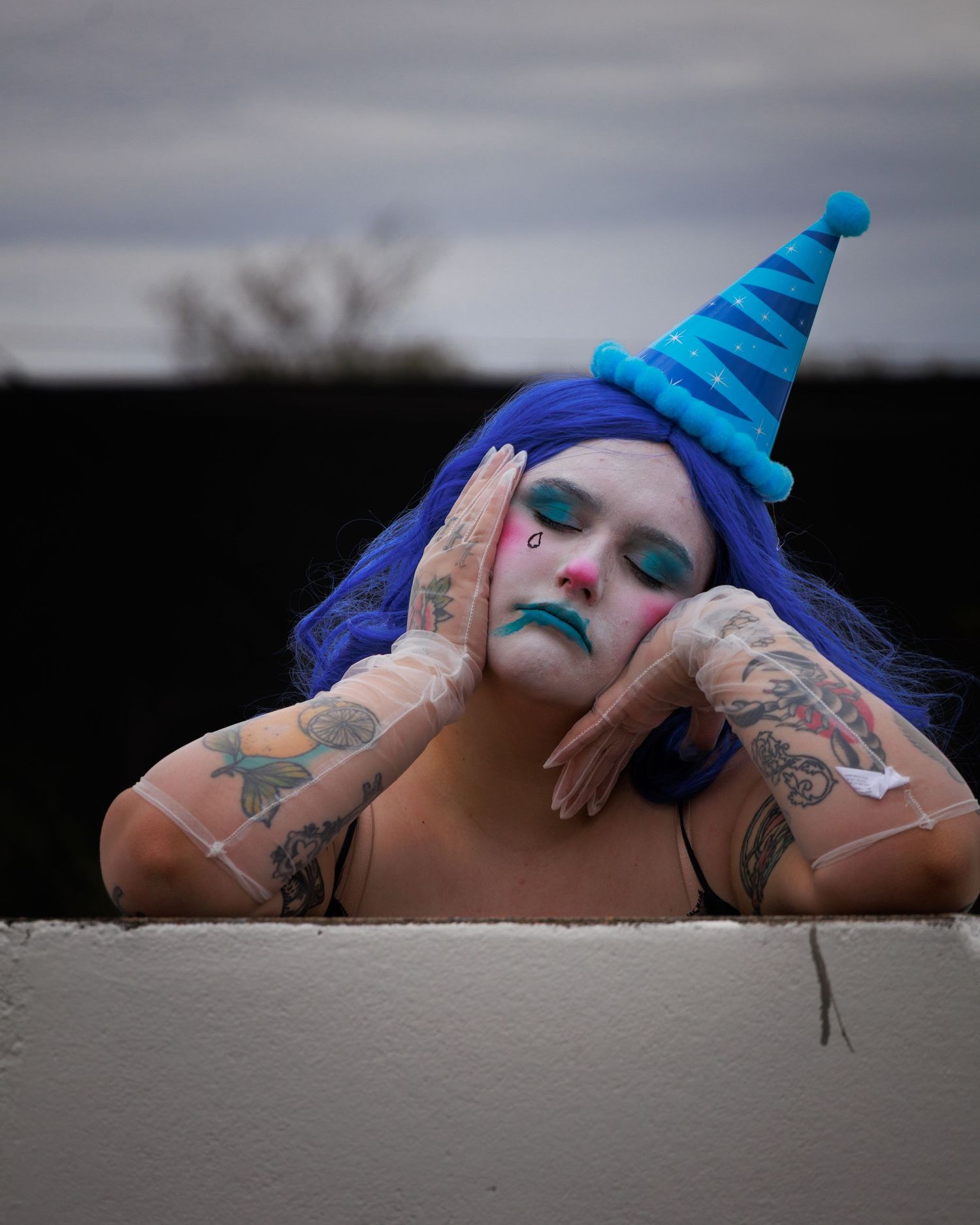 A person with blue hair and tattoos poses dramatically on a white wall in multiple artistic shots.
