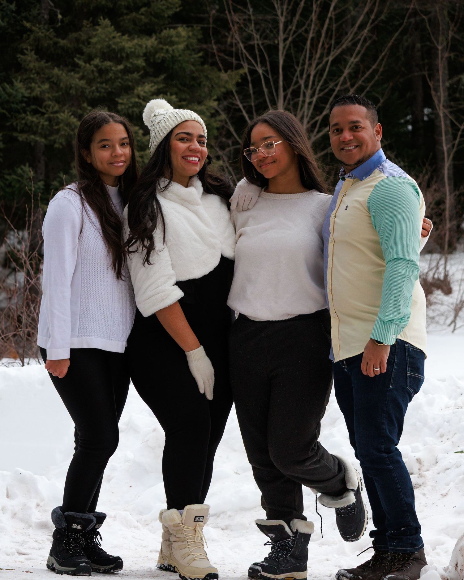 Winter group photo of four friends standing together in the snow wearing casual outfits.