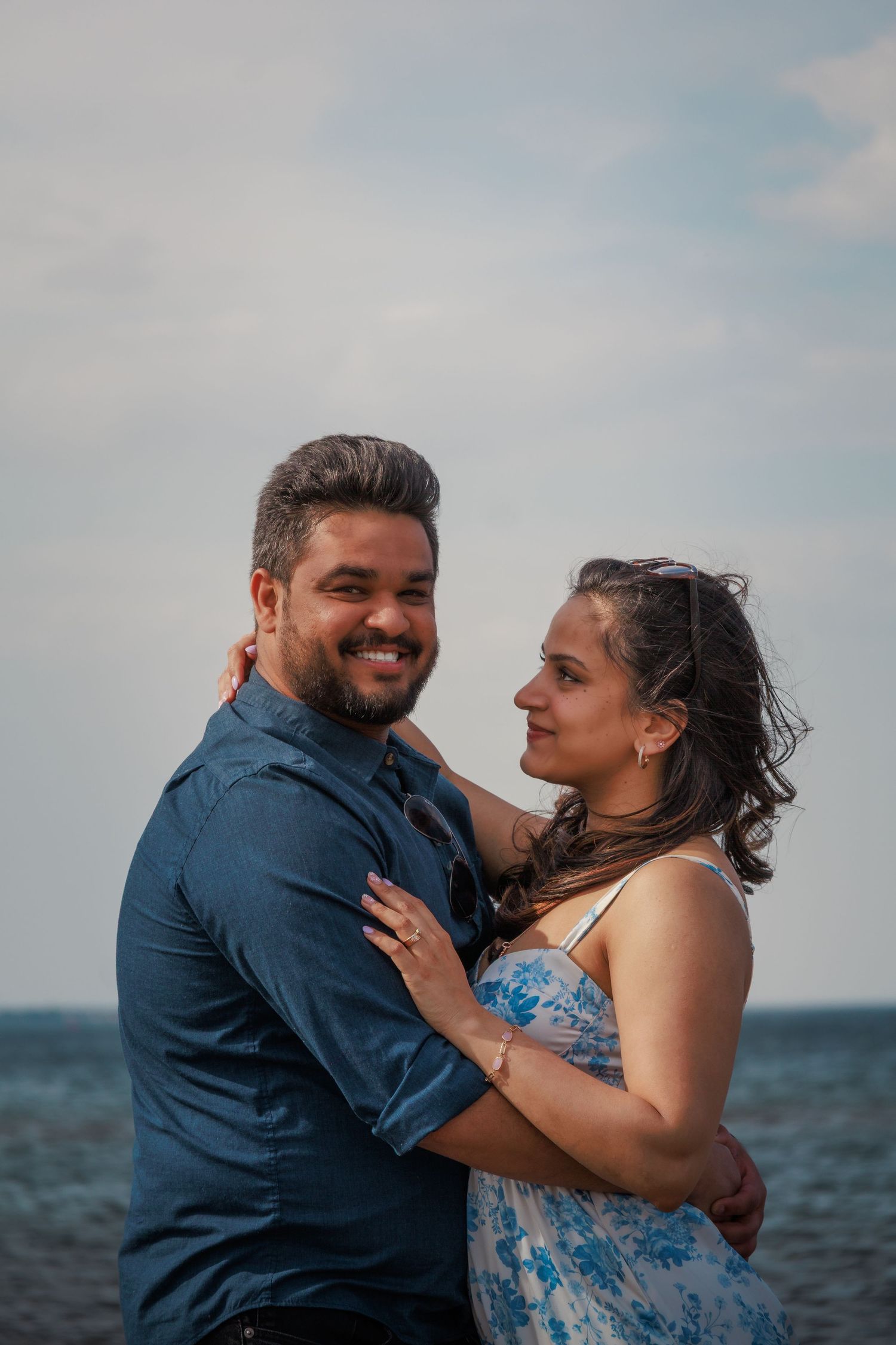 A happy couple laughs and embraces while standing together on a sunny beach.