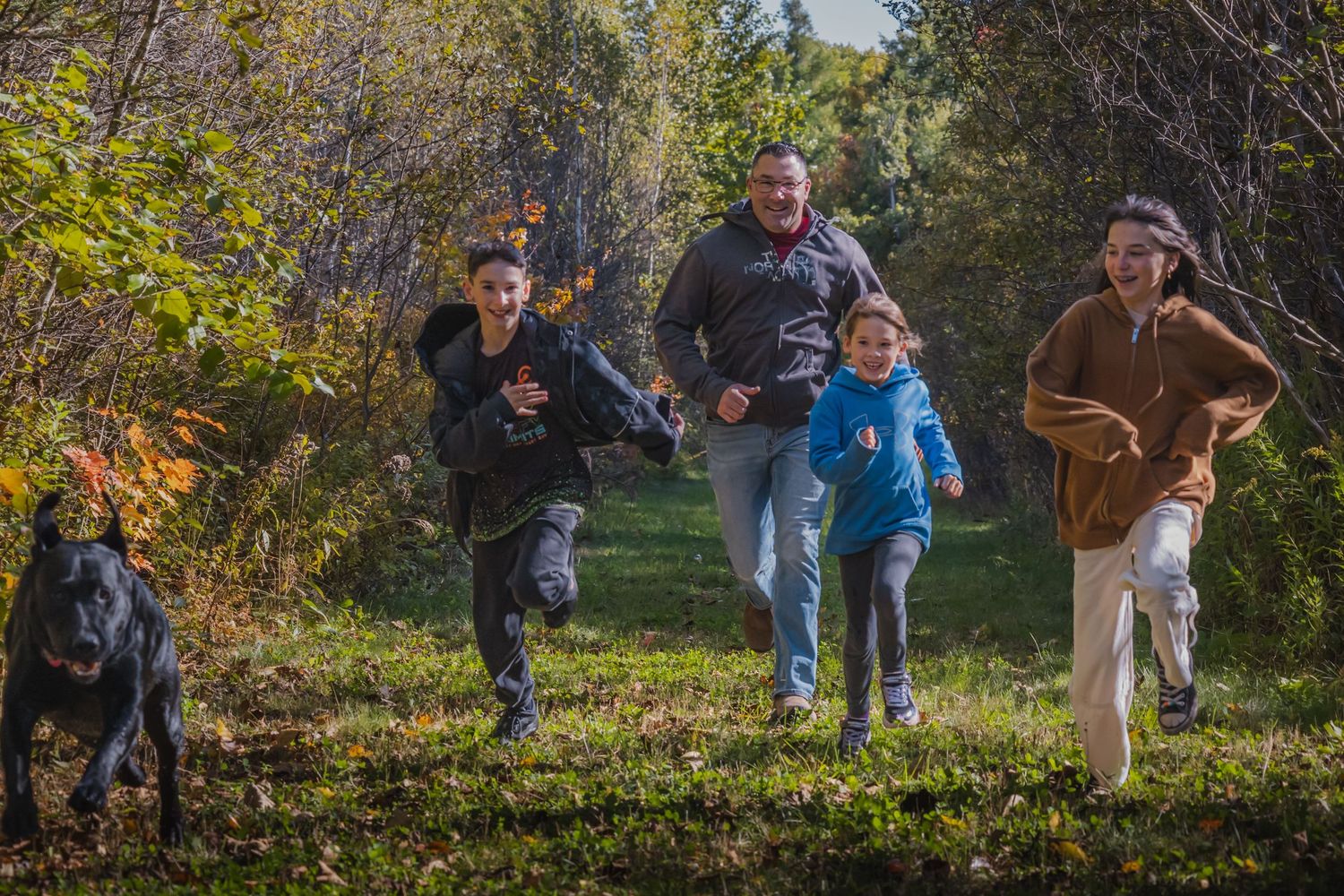 Action shot of family and dog running together on autumn forest trail.