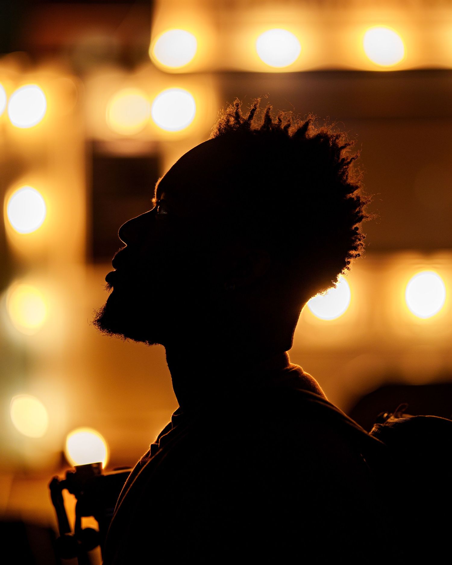 Dramatic silhouette of a man with curly hair against warm glowing bokeh lights in golden tones.