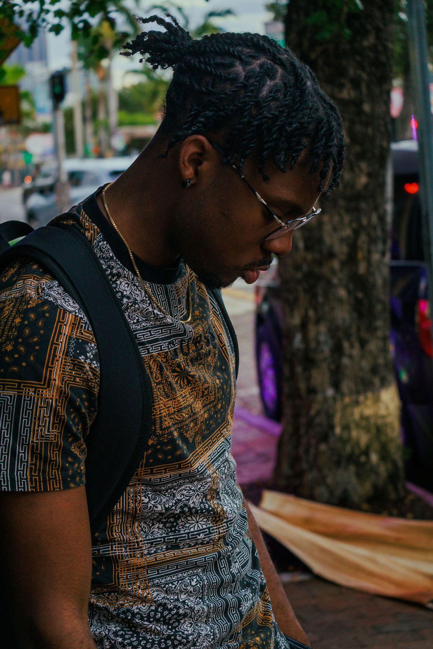 A person wearing a patterned black and gold shirt sits outdoors in an urban setting.