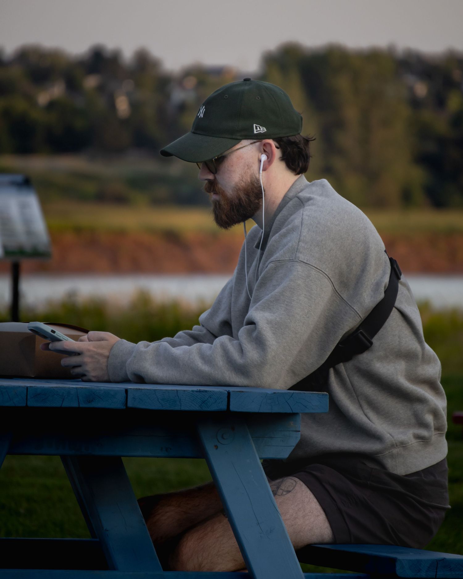 Person sitting on blue bench outdoors wearing grey sweatshirt and baseball cap.