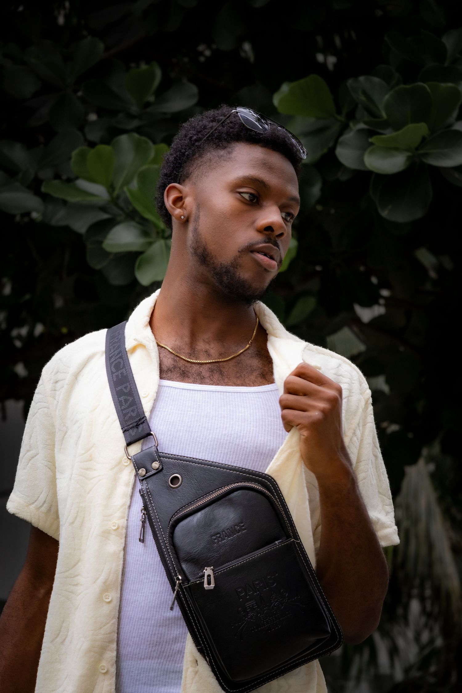 Person wearing yellow button-up shirt and white tank top adjusts black crossbody bag.