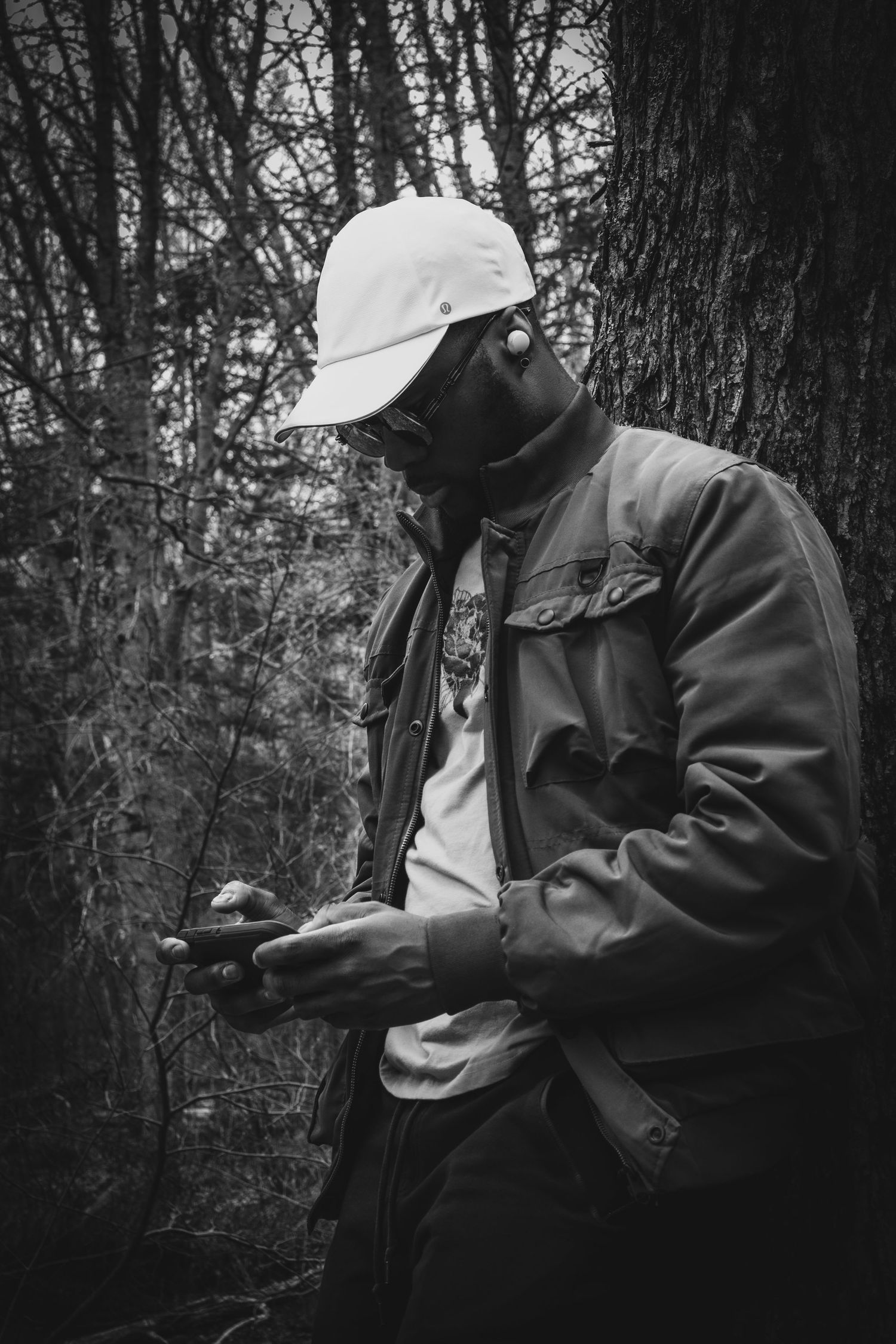 Monochrome photo of person in white cap and jacket standing against forest backdrop.