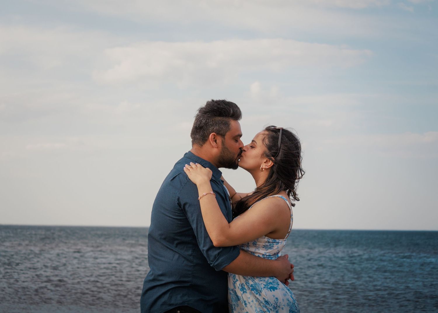 Romantic couple embracing by ocean during sunset photoshoot.