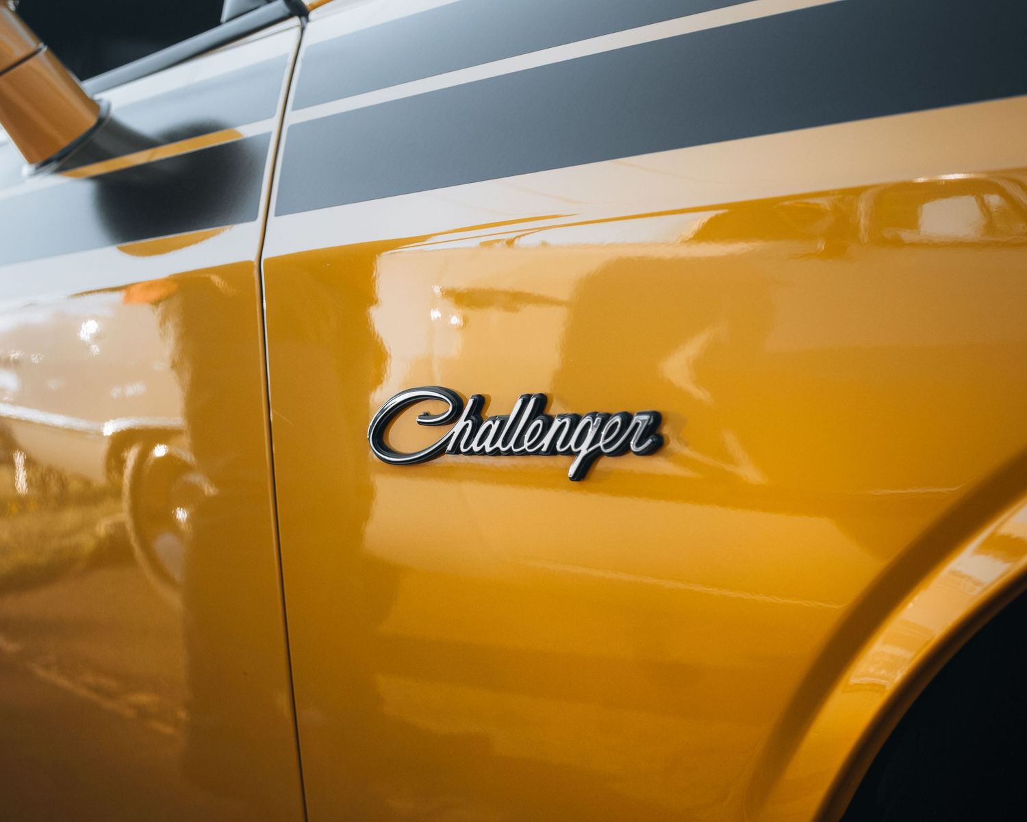 Close-up of a yellow Dodge Challenger car badge emblem on the golden muscle car door panel.