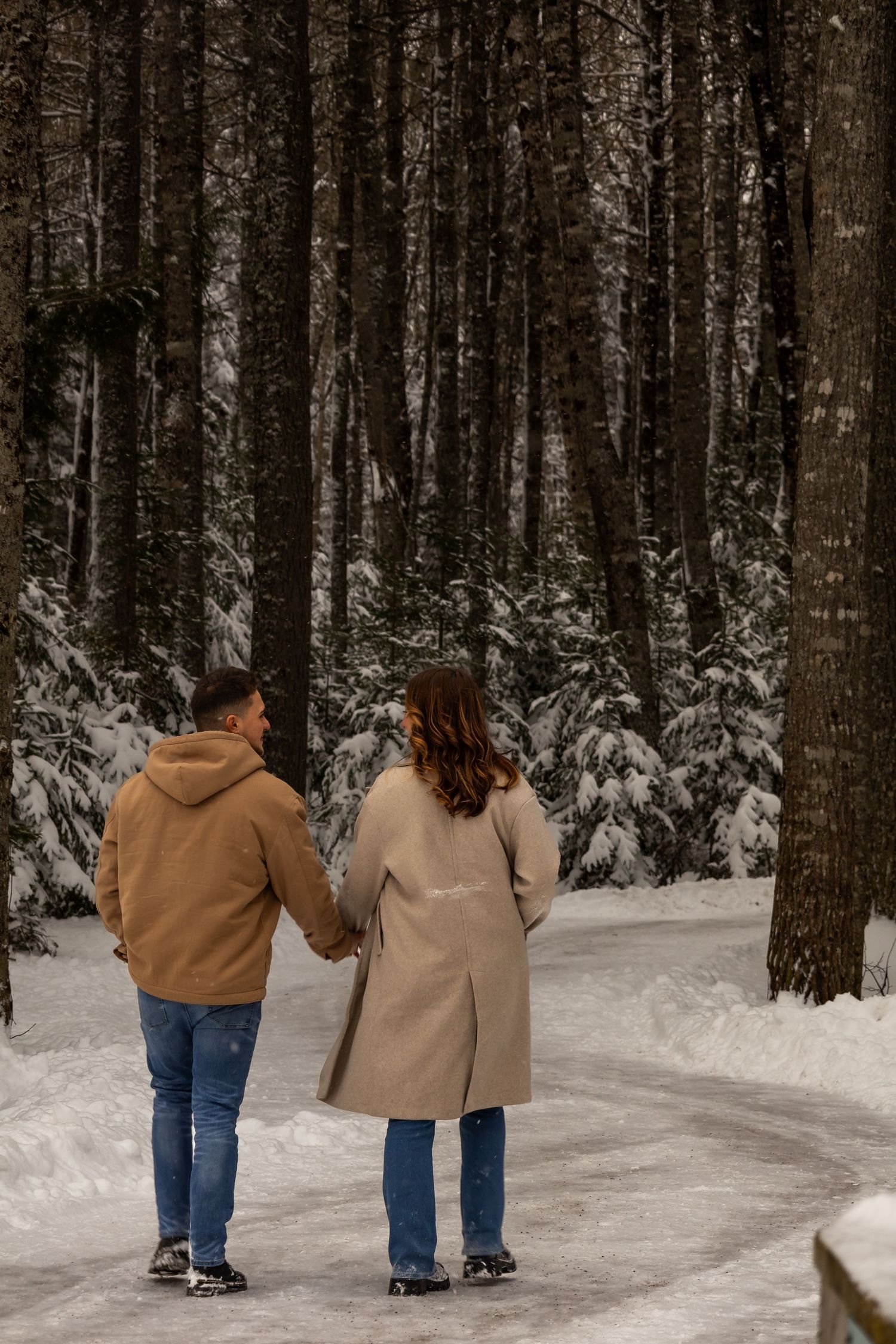 Couple walking hand in hand through a snow-covered forest path.