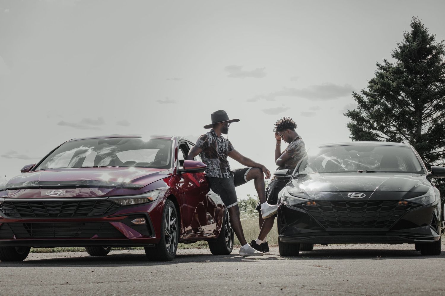 Group posing with luxury sports cars on overcast day.