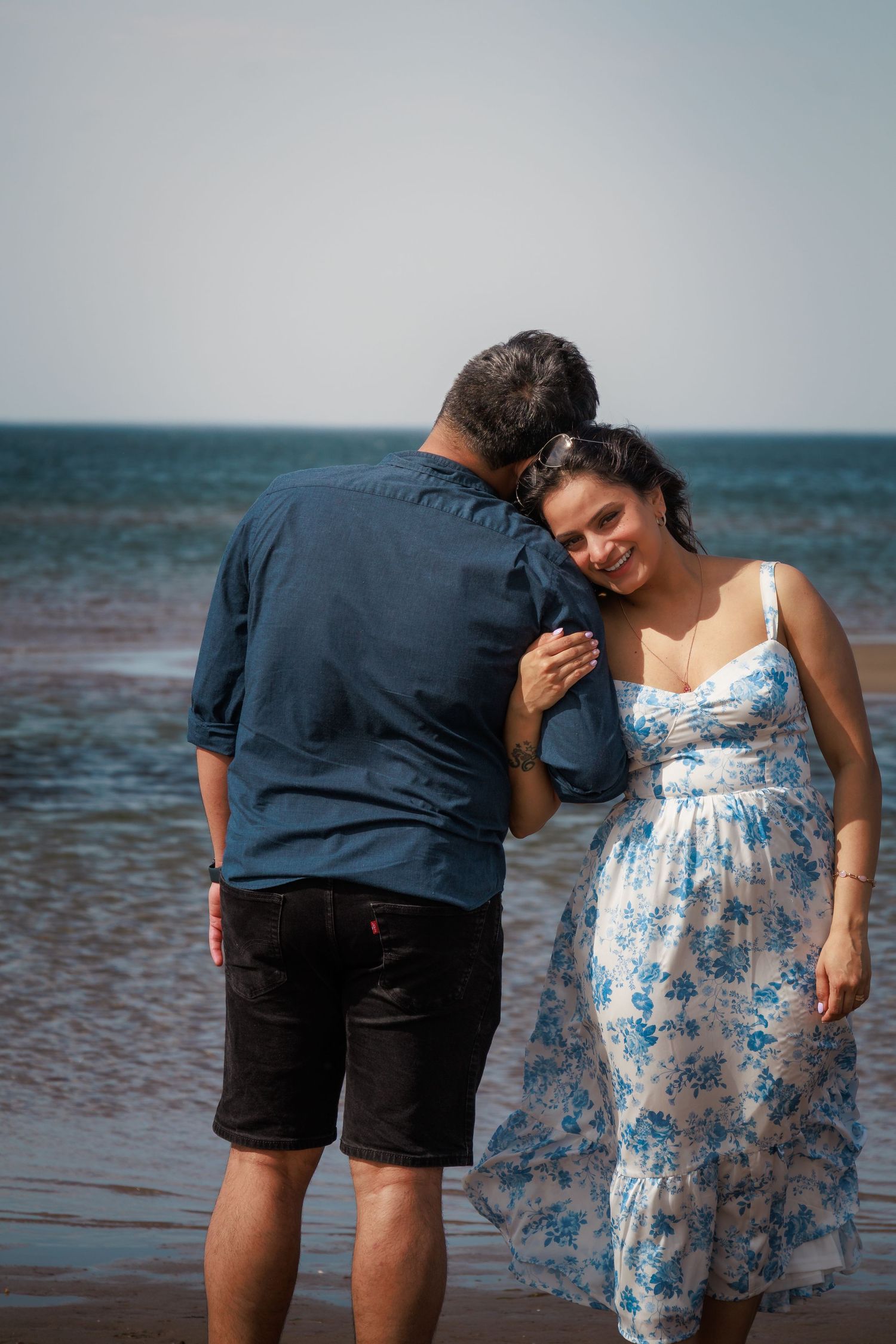 A couple shares tender moments together by the ocean, with waves visible in the background.