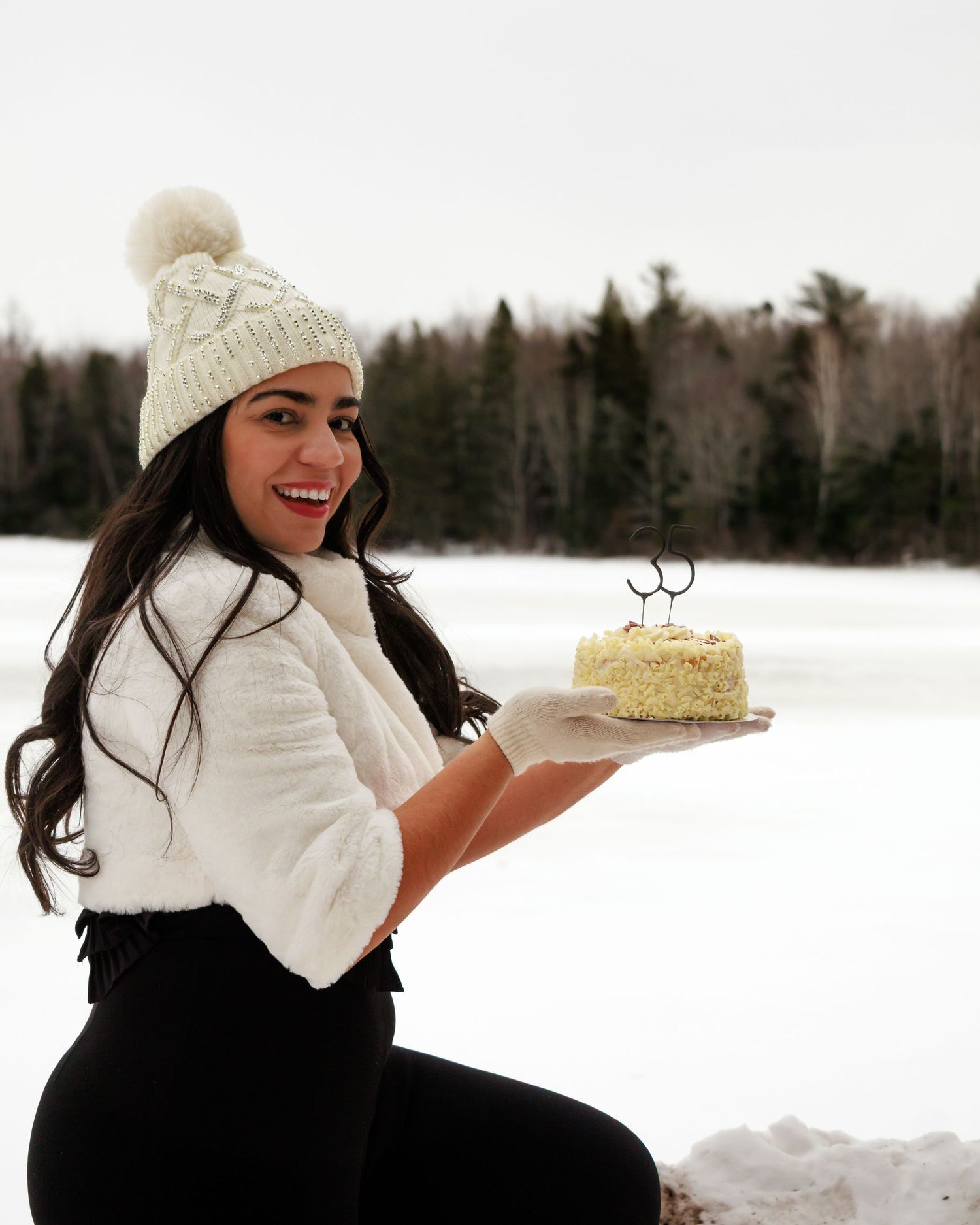 Person in white winter clothing holds dessert plate while sitting in snowy landscape.