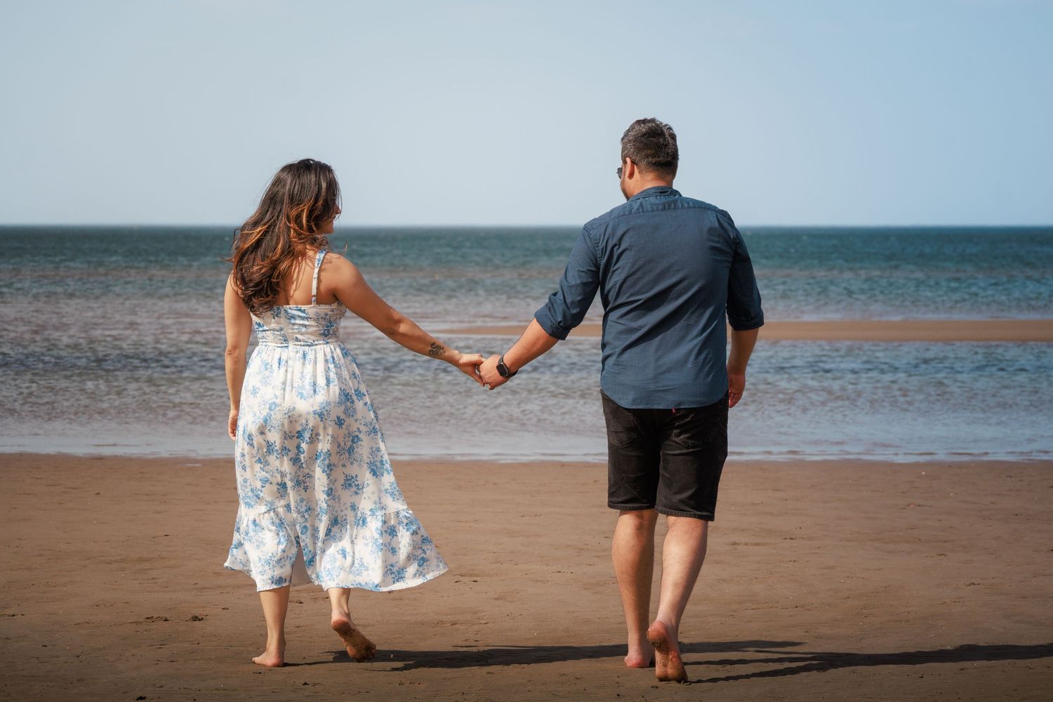 Couple walking hand in hand along beach shoreline at sunset.