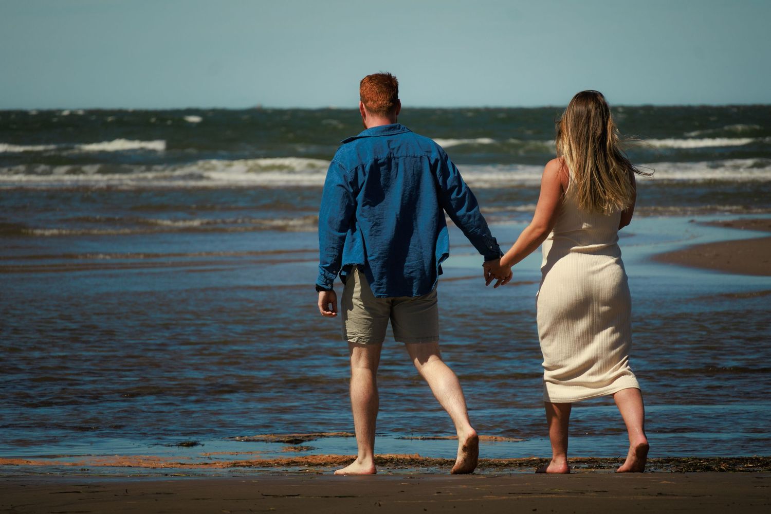 Couple holding hands while walking along the shoreline at sunset on a beach.