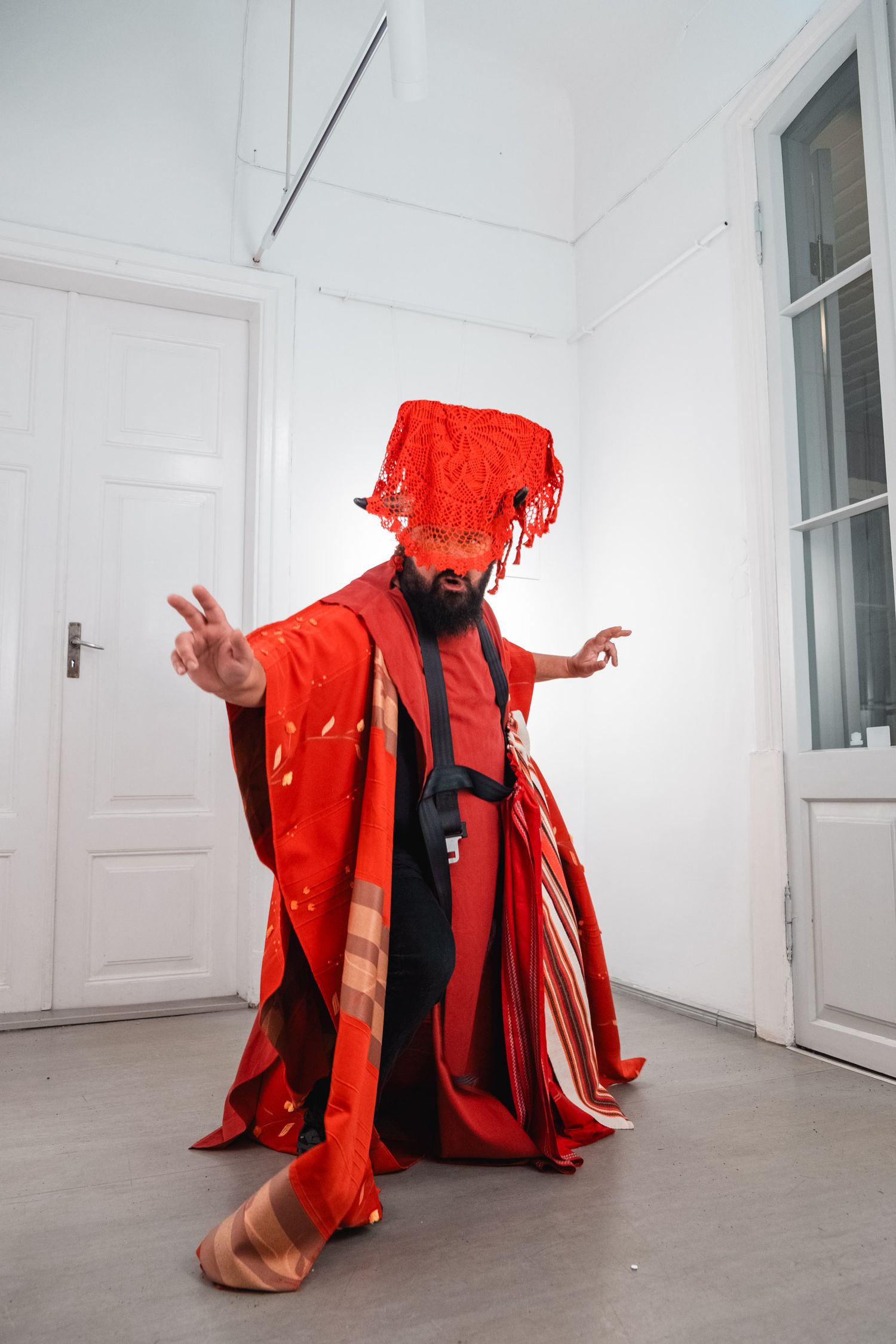 Performance art scene with figure in flowing red costume and headdress.