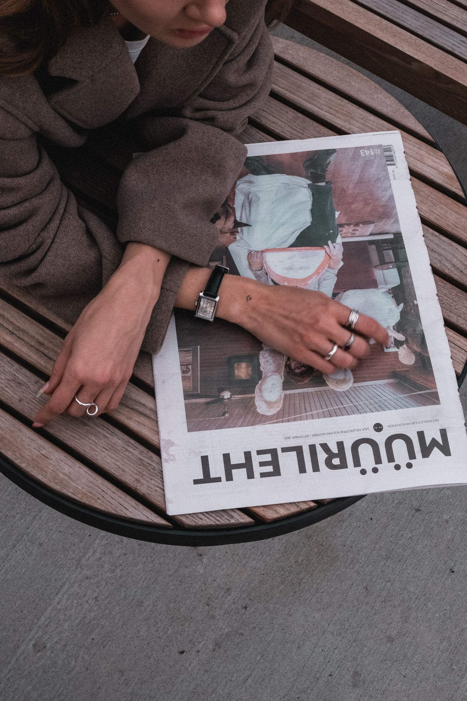 Hands holding and browsing through a magazine on wooden bench surface.