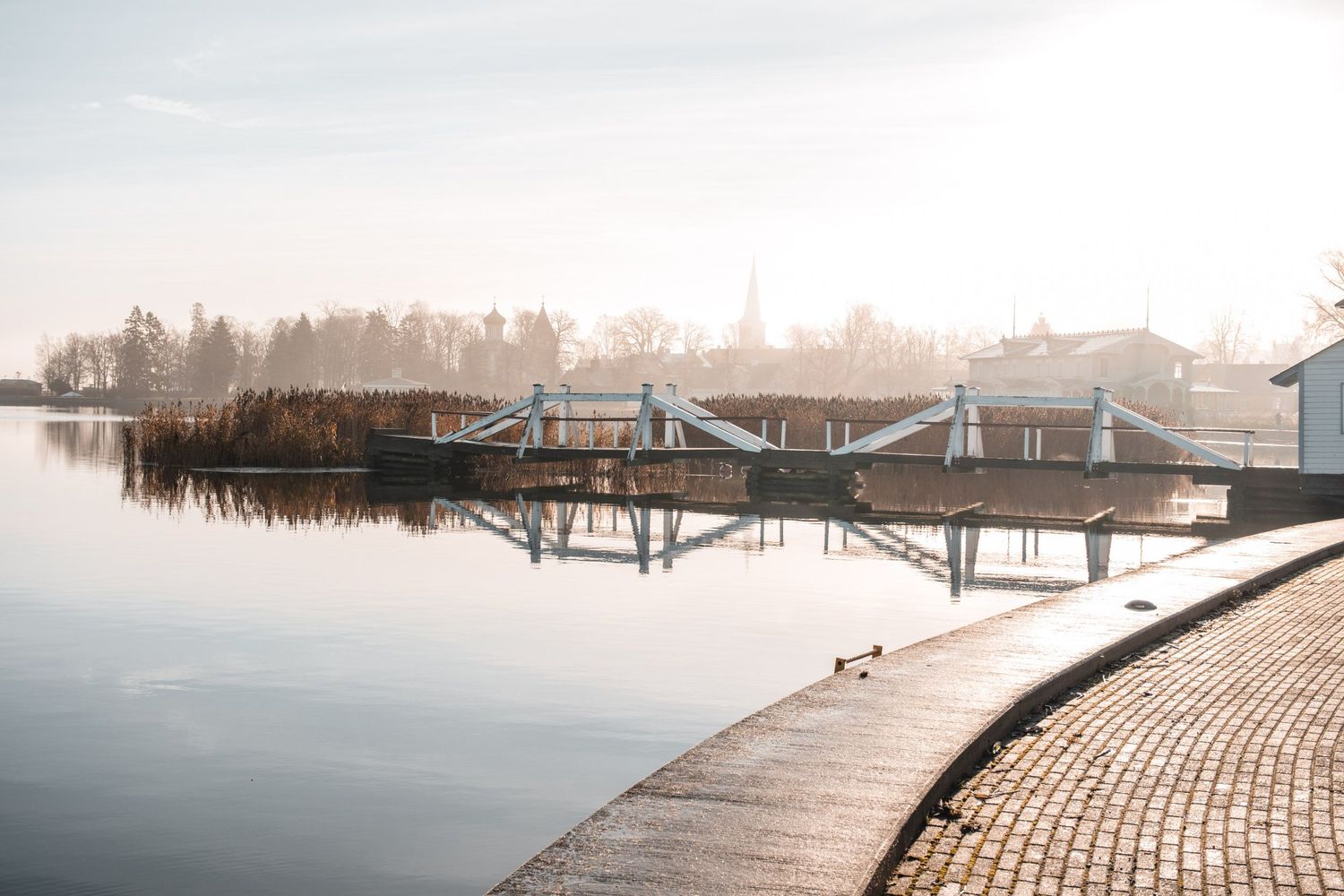 Serene waterfront view of modern boathouses with reflections on calm lake at sunset.