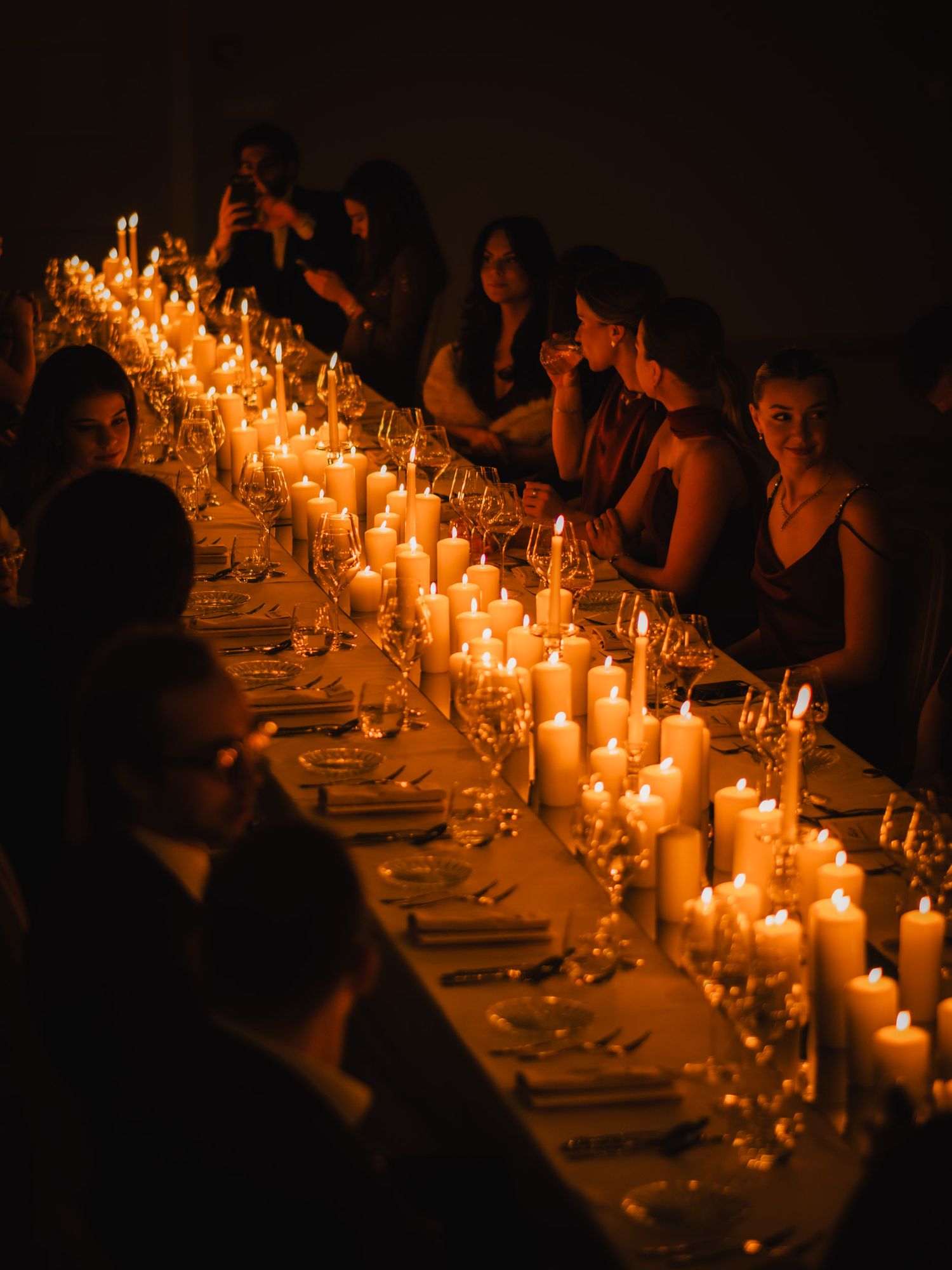 A candlelit dinner table with glowing candles illuminating a long dining setup in a dark, intimate setting.